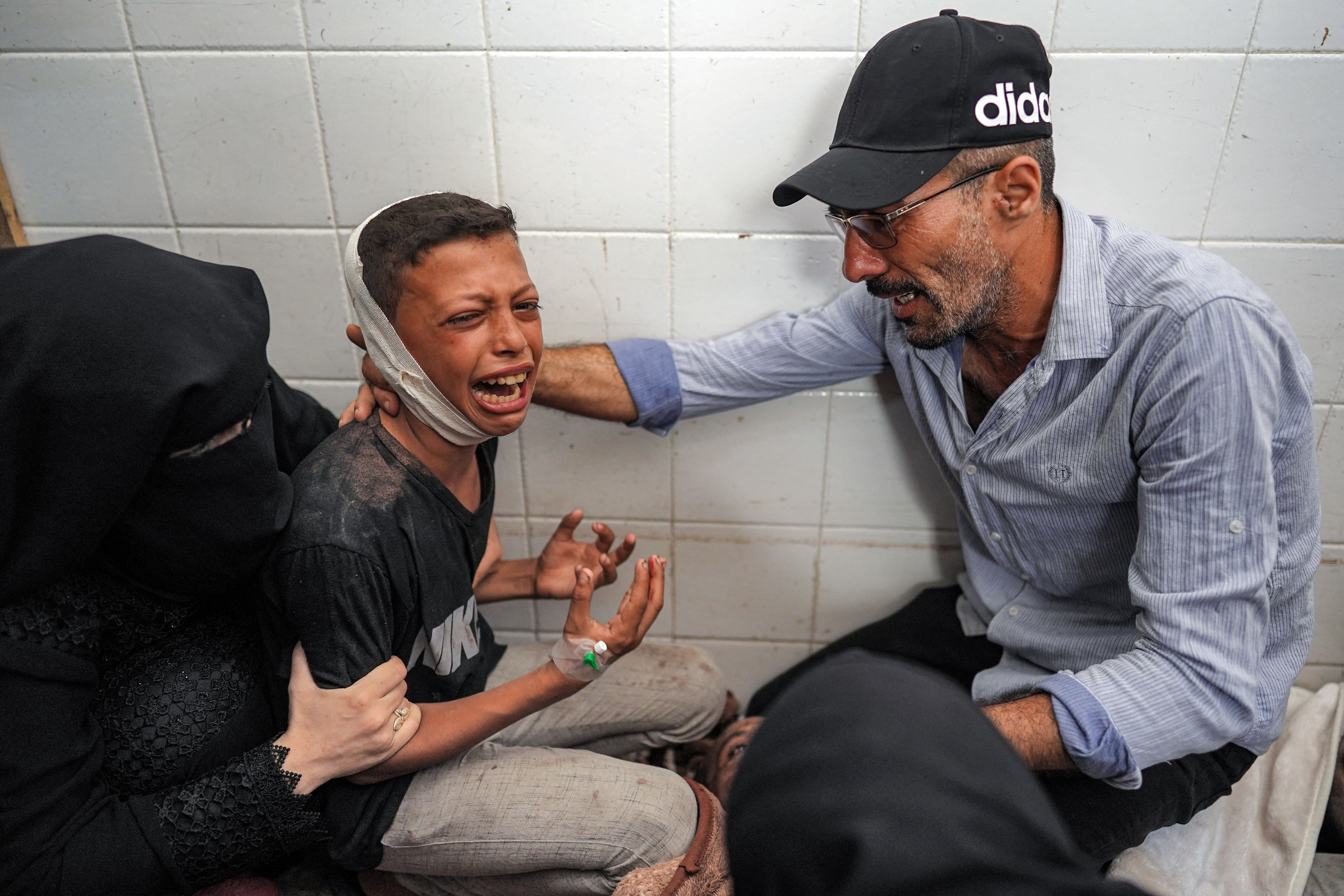 A woman and a man comfort an injured boy mourning the loss of his father who was killed in the aftermath of overnight Israeli bombardment in al-Maghazi