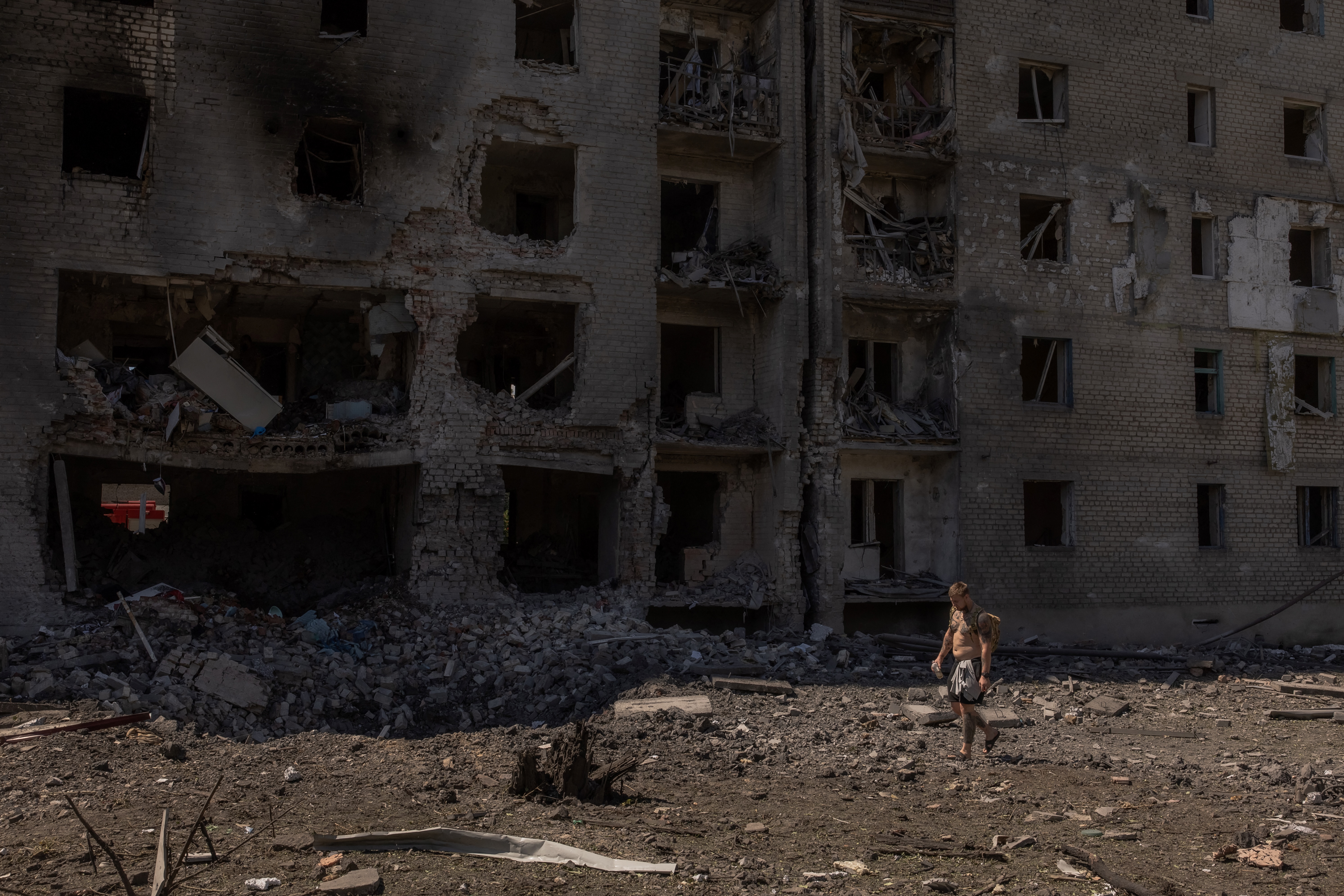 A man walking past an apartment block after a Russian attack on Selydove in eastern Donetsk. The apartment block is badly damaged. There is a huge crater on the ground.