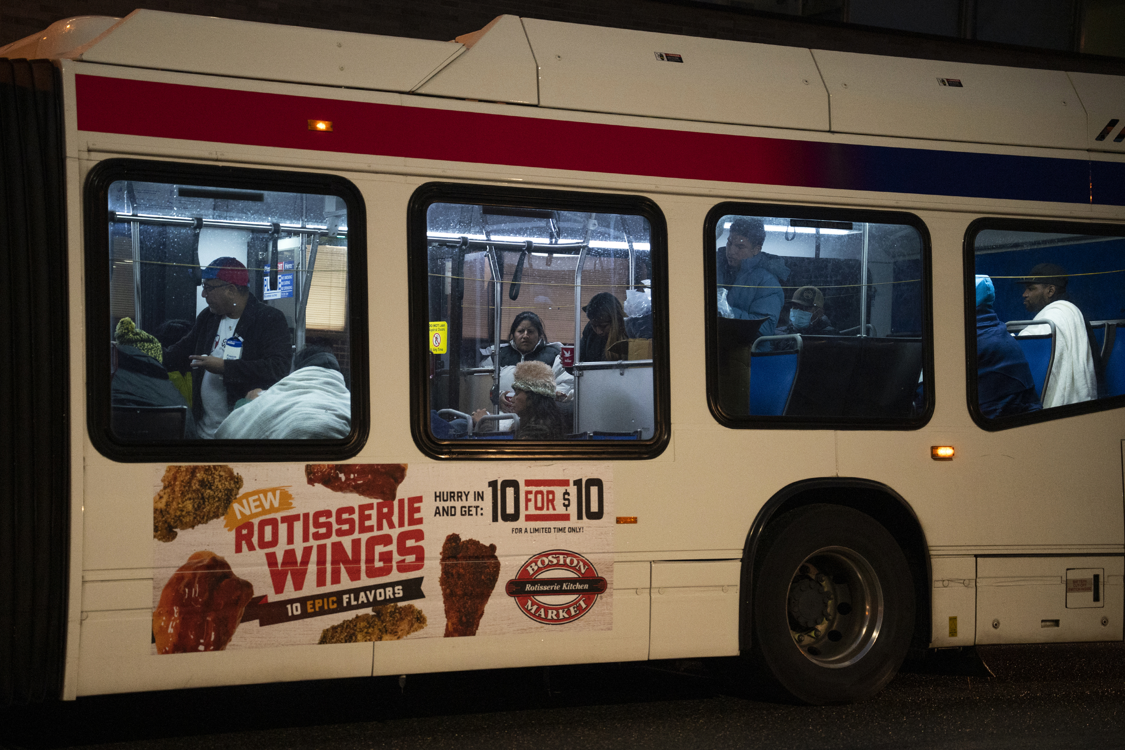 A bus with an advertisement for rotisserie wings on the side arrives in Philadelphia carrying migrants and asylum seekers.