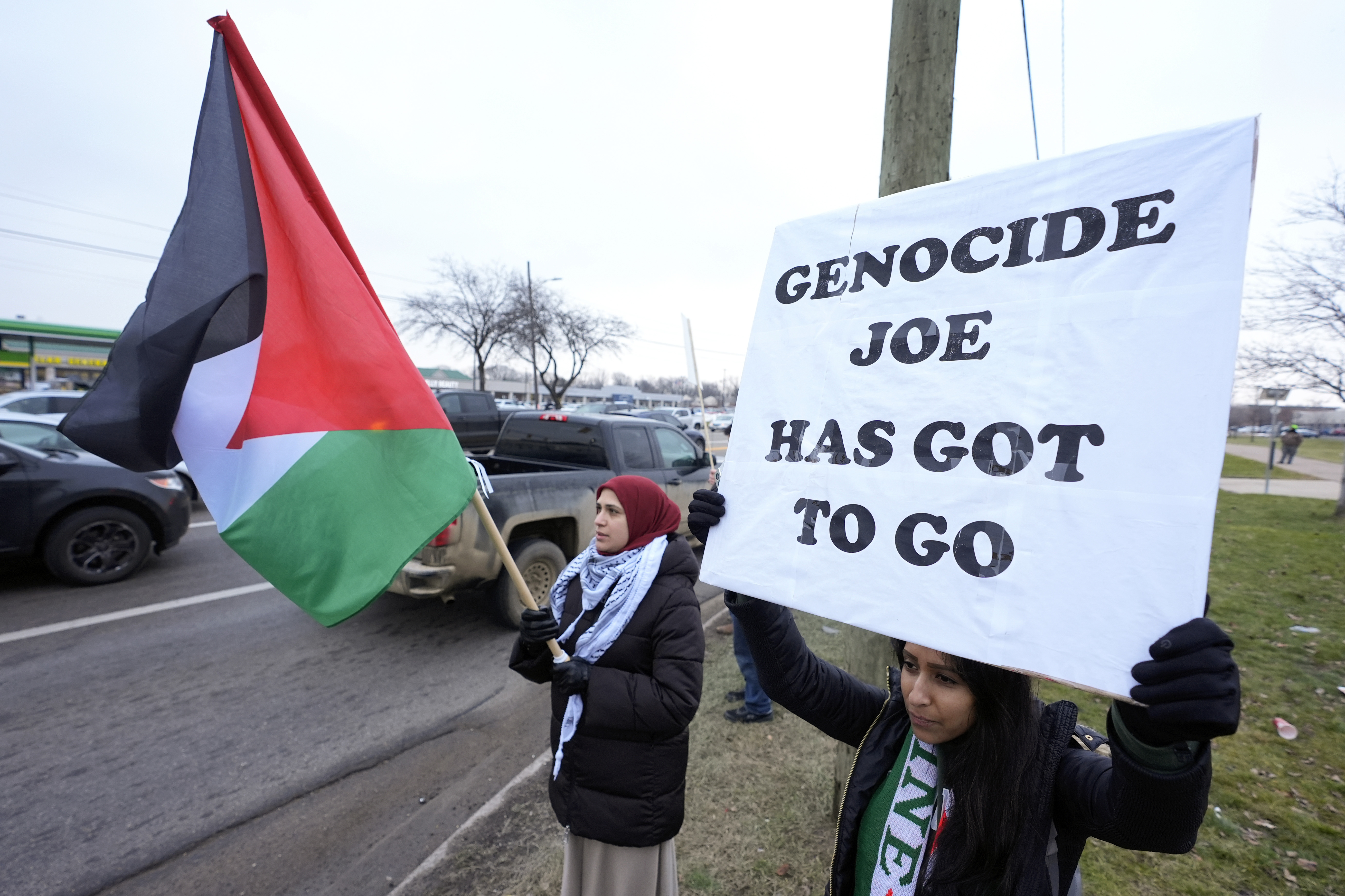 Protesters on the side of a US road wave a Palestine flag and hold up a sign, "Genocide Joe has got to go."