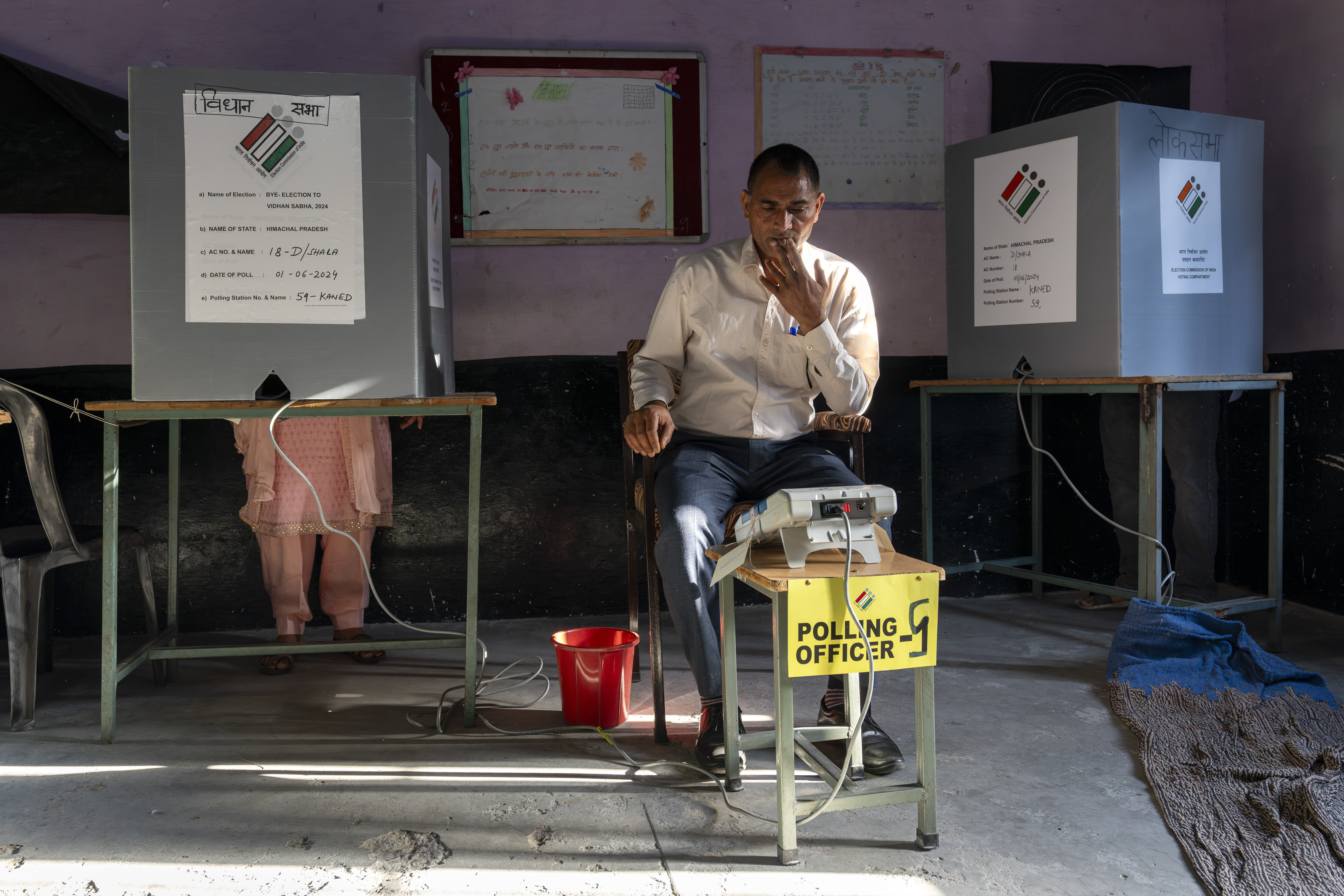 A polling official looks at his device for confirmation as a voter casts her vote in a bye-election after voting in the seventh and last round of polling in India's national election in Dharamshala, Saturday, June 1