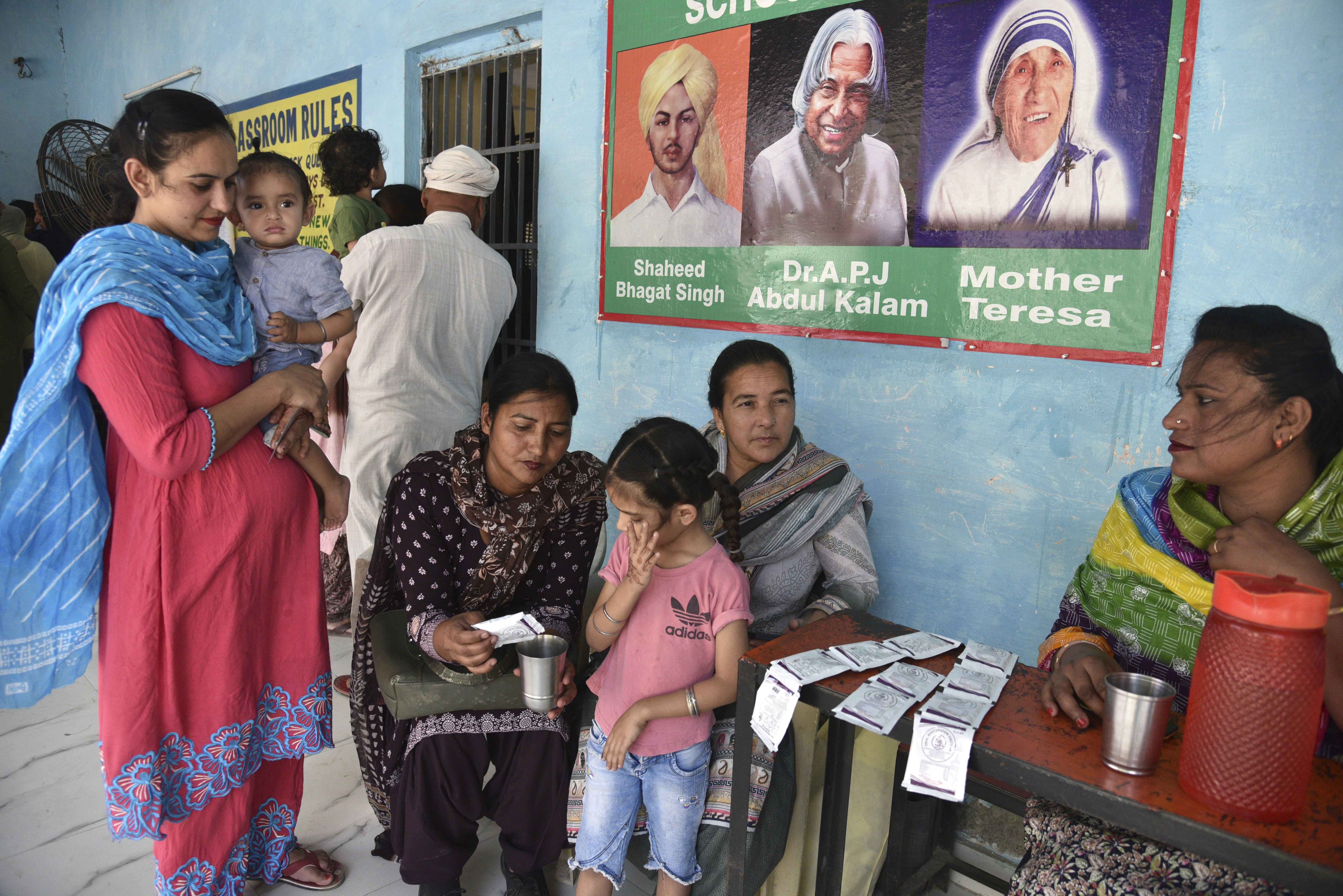A woman volunteer prepares an oral re-hydration solution for a child as her parents wait to cast their vote on a hot summer day during the seventh and the last phase of general election, near Amritsar, India, Saturday, June 1