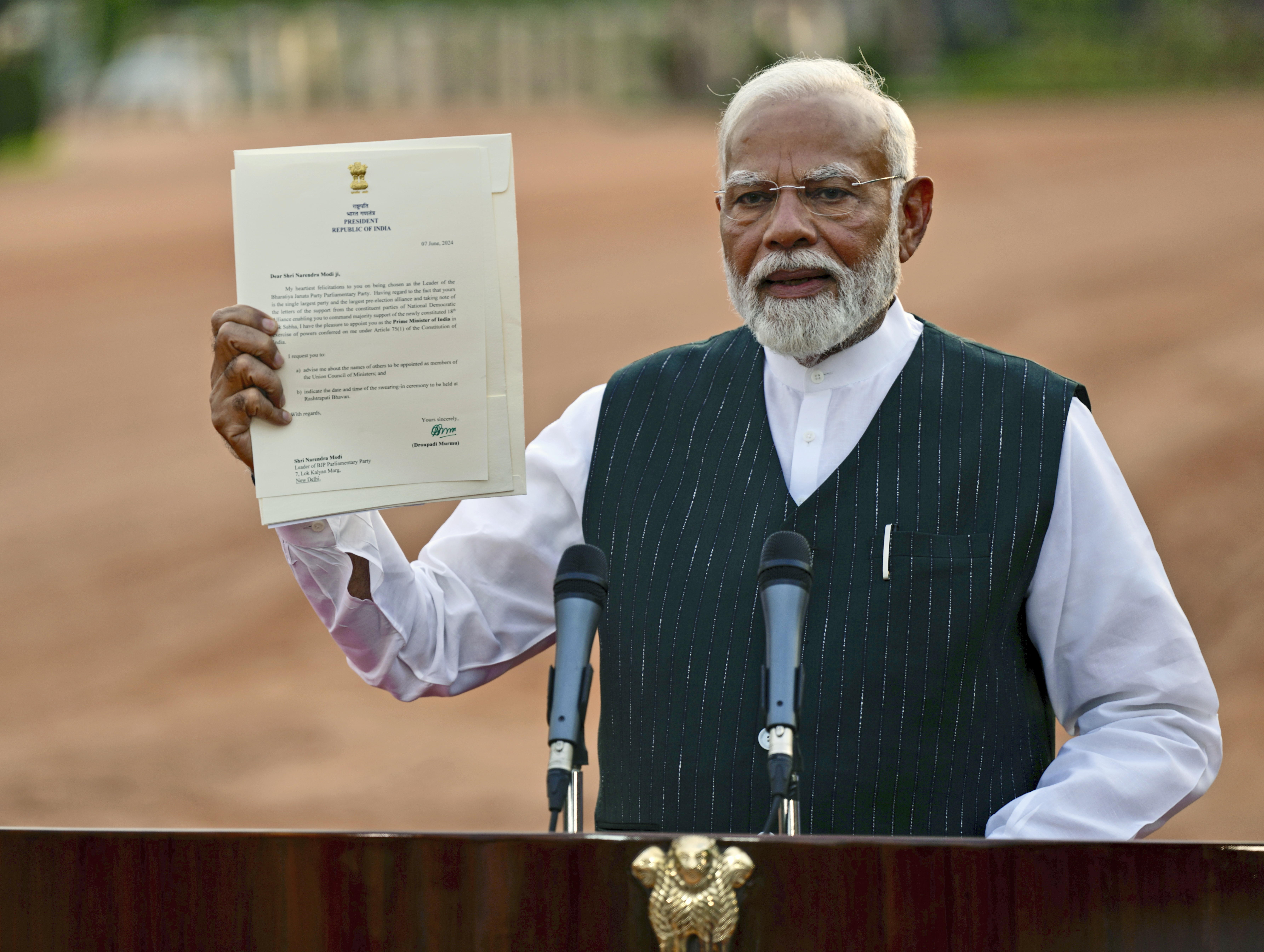 Indian Prime Minister Narendra Modi displays a letter from the President of India, Draupadi Murmu, inviting him to form the next central government, outside the Rashtrapati Bhavan in New Delhi, India, Friday, June 7, 2024. (AP Photo/Manish Swarup)
