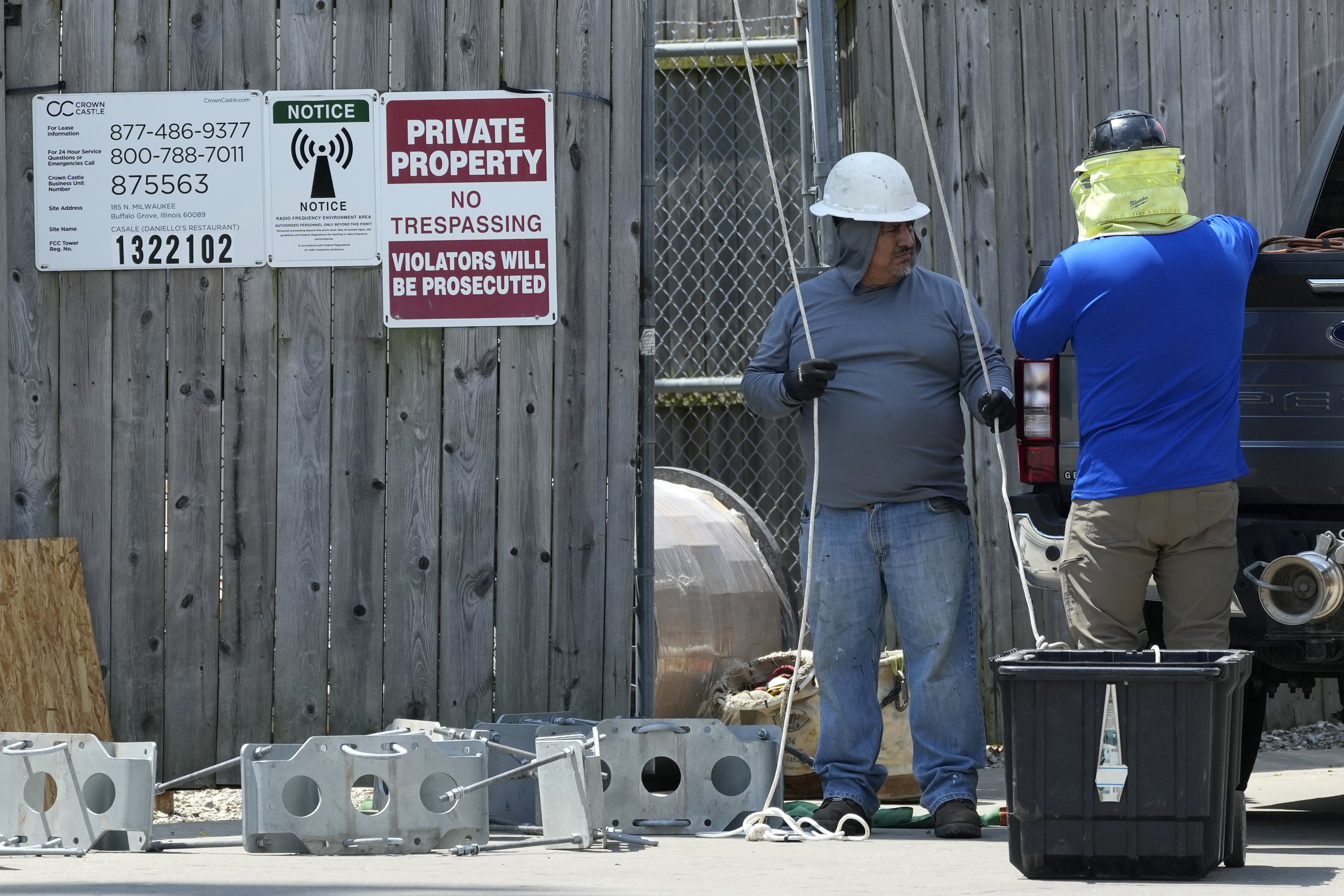 Construction workers stand outside a wooden fence in hard hats.