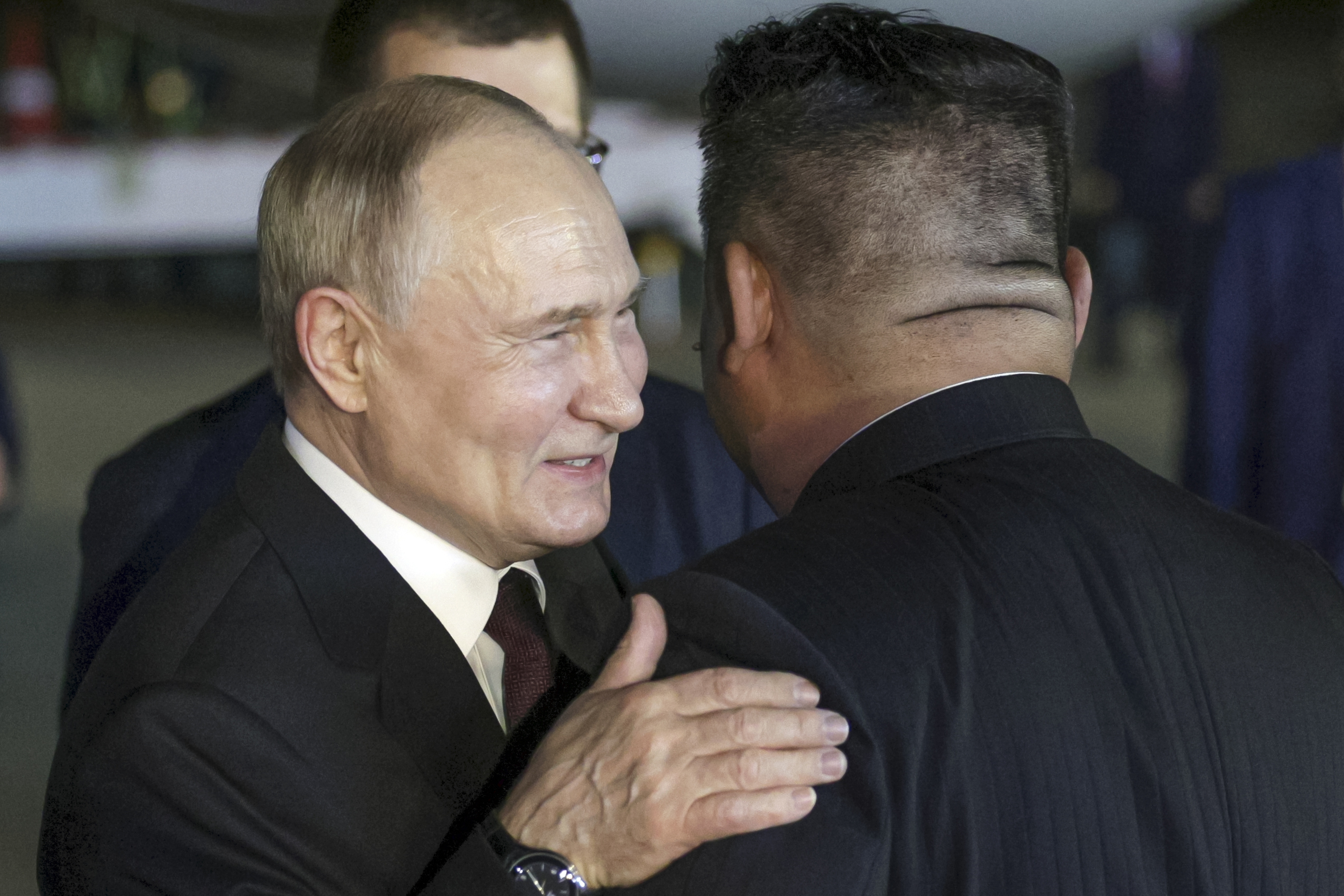 Putin and Kim Jong Un embrace at the airport. Putin is smiling. Kim has his back to the camera