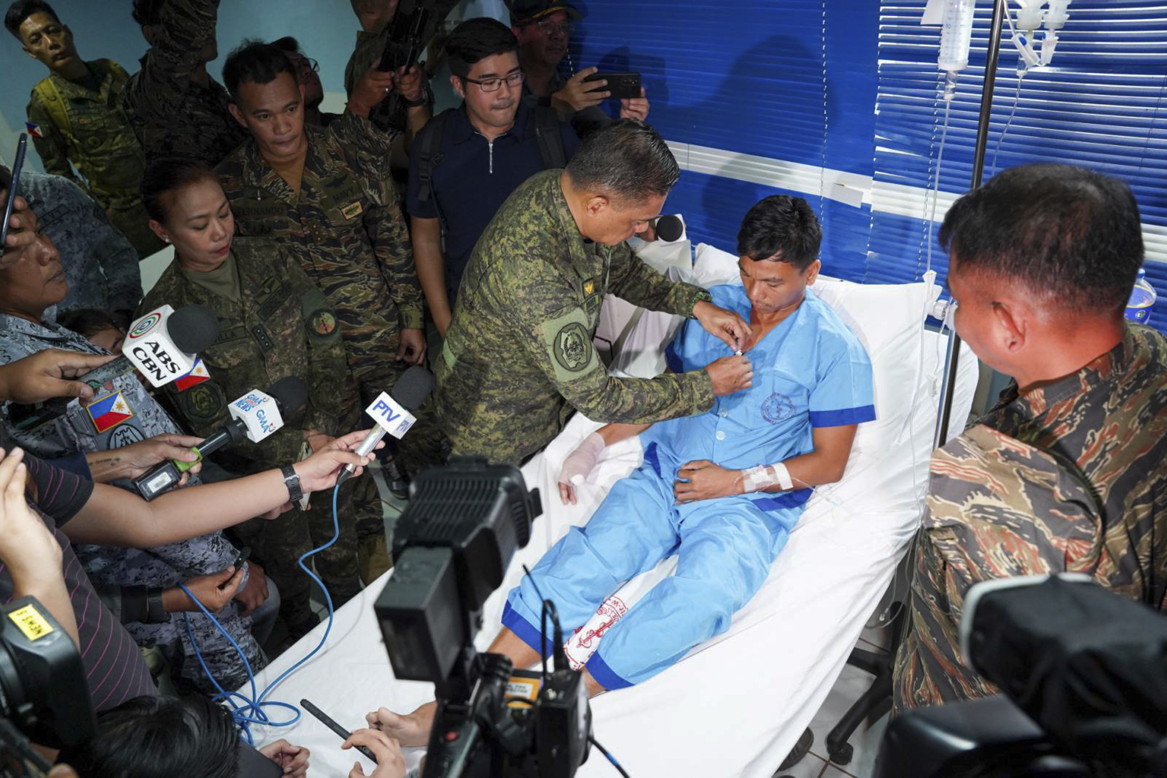 Philippine military chief General Romeo Brawner pins a medal on sailor who was taken to hospital after a confrontation with the Chinese Coast Guard. The sailor is lying on a hospital bed in a sky blue hospital pyjamas. His right hand and wrist is bandaged. 