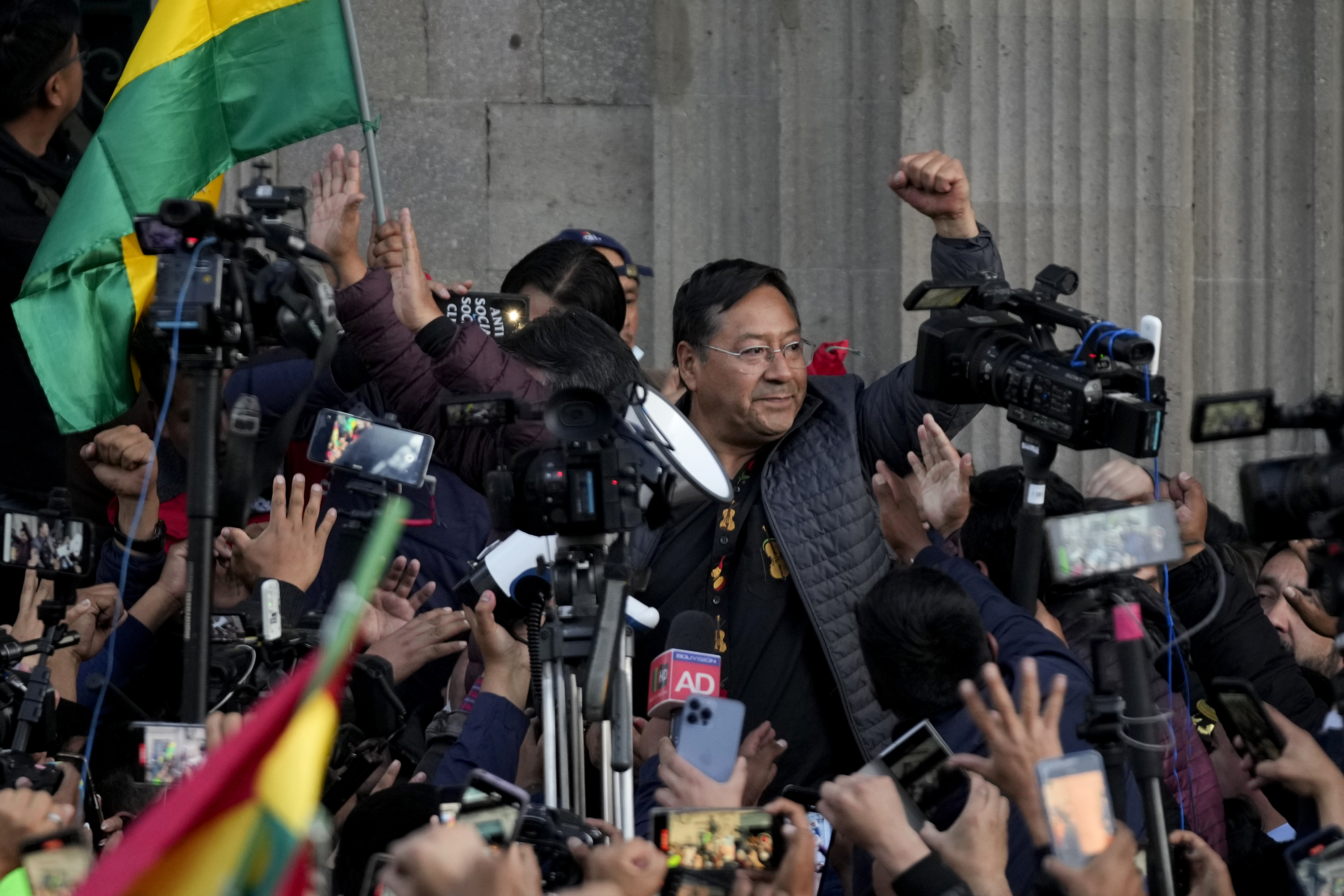 Bolivian President Luis Arce raises a clenched fist surrounded by supporters and media, outside the government palace in La Paz, Bolivia, 
