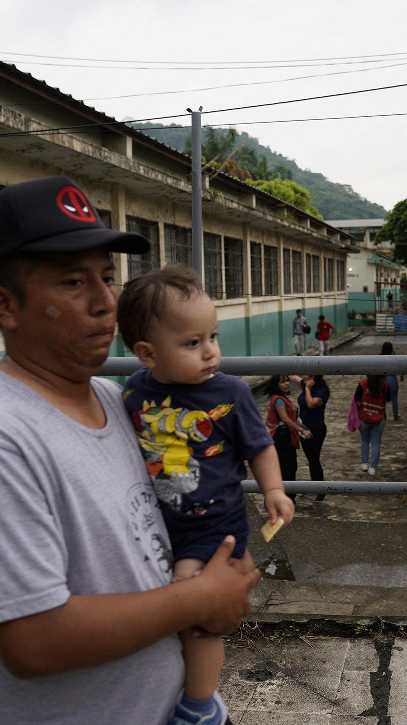 A man with a baby in his arms walks past a soldier on an elevated walkway.