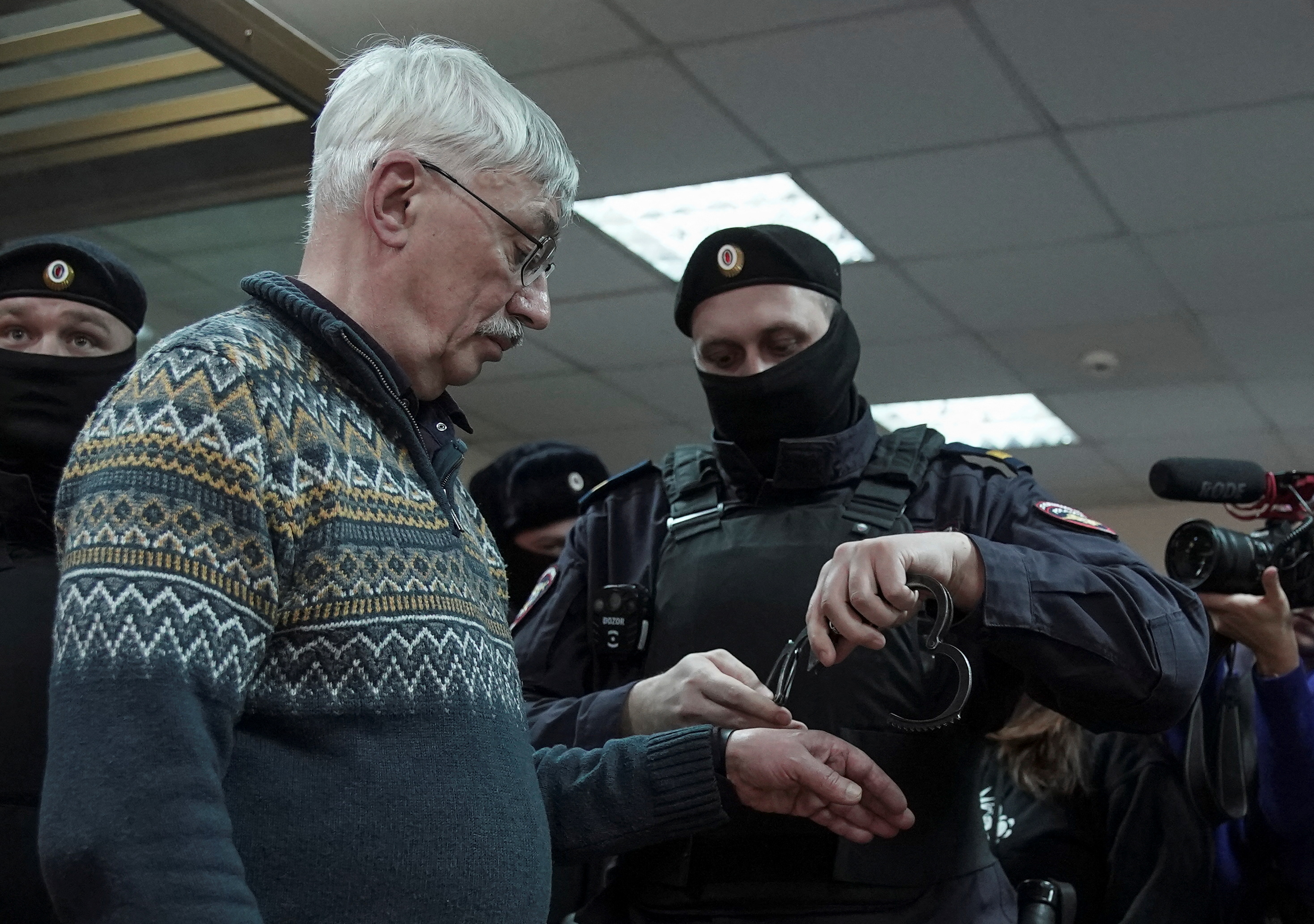 A police officer puts handcuffs on Russian veteran human rights campaigner Oleg Orlov
