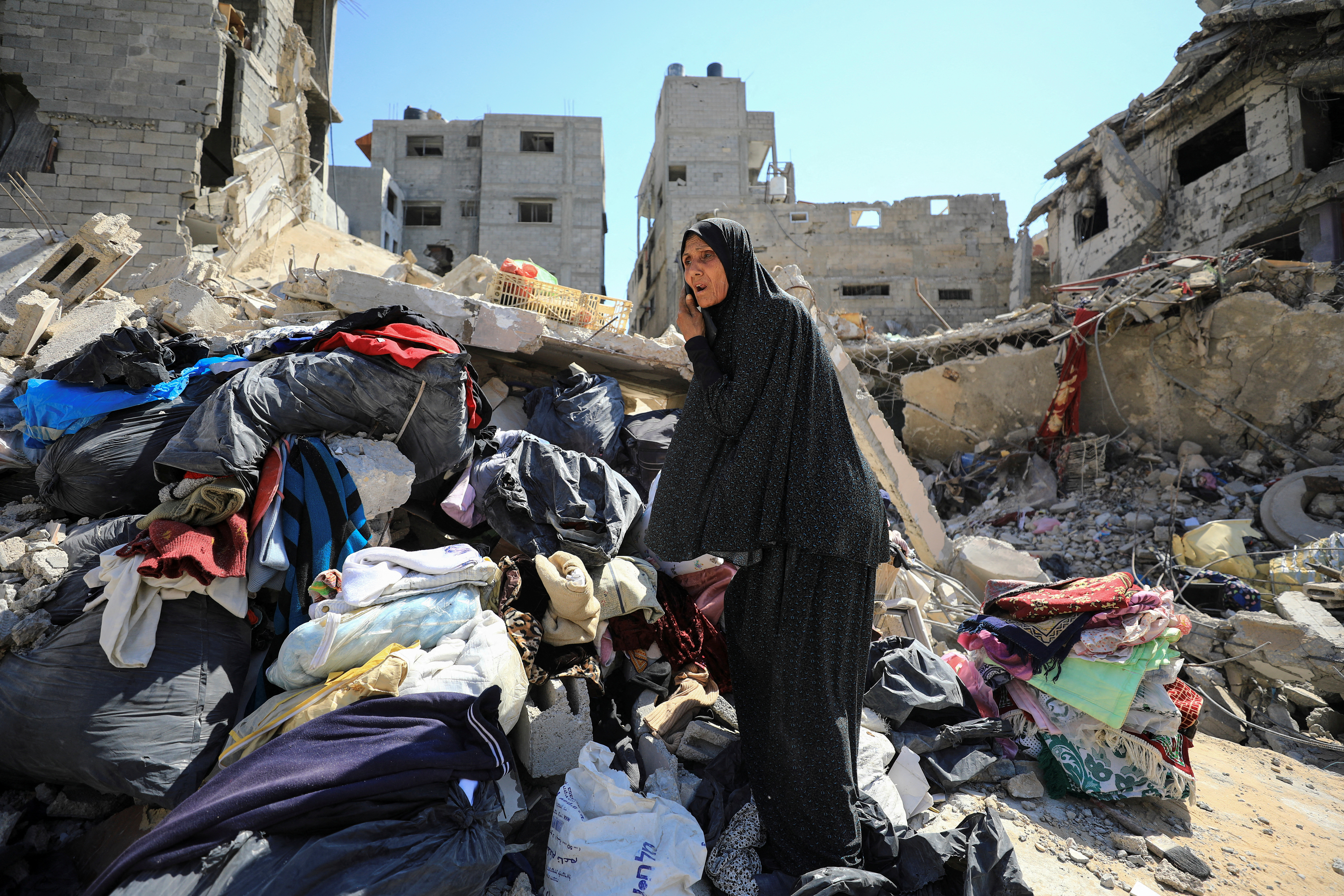 a woman stands on a pile of rubbish next to destroyed buildings