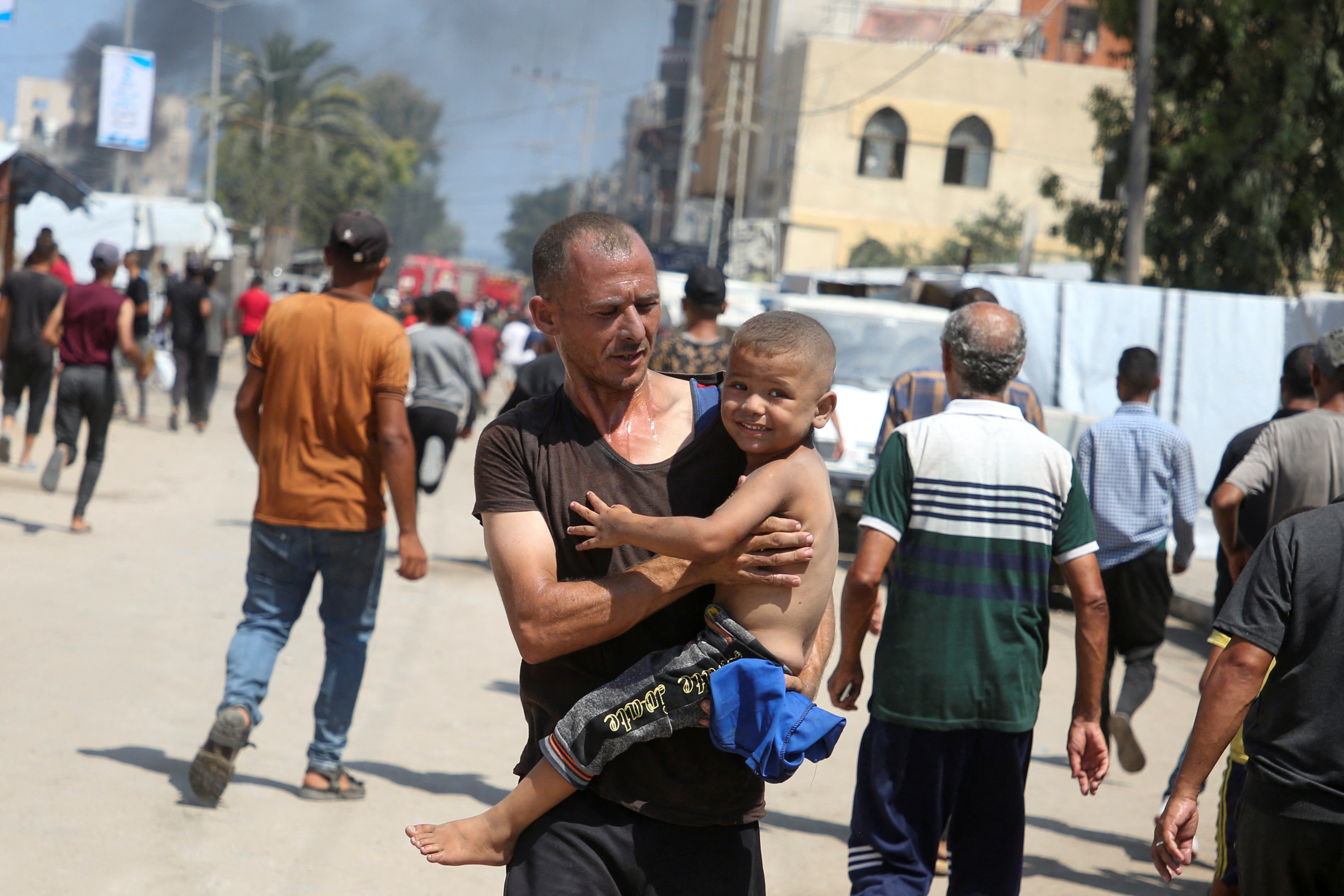 A man carries a child at the site of what Palestinians say was an Israeli strike at a tent camp in Al-Mawasi area