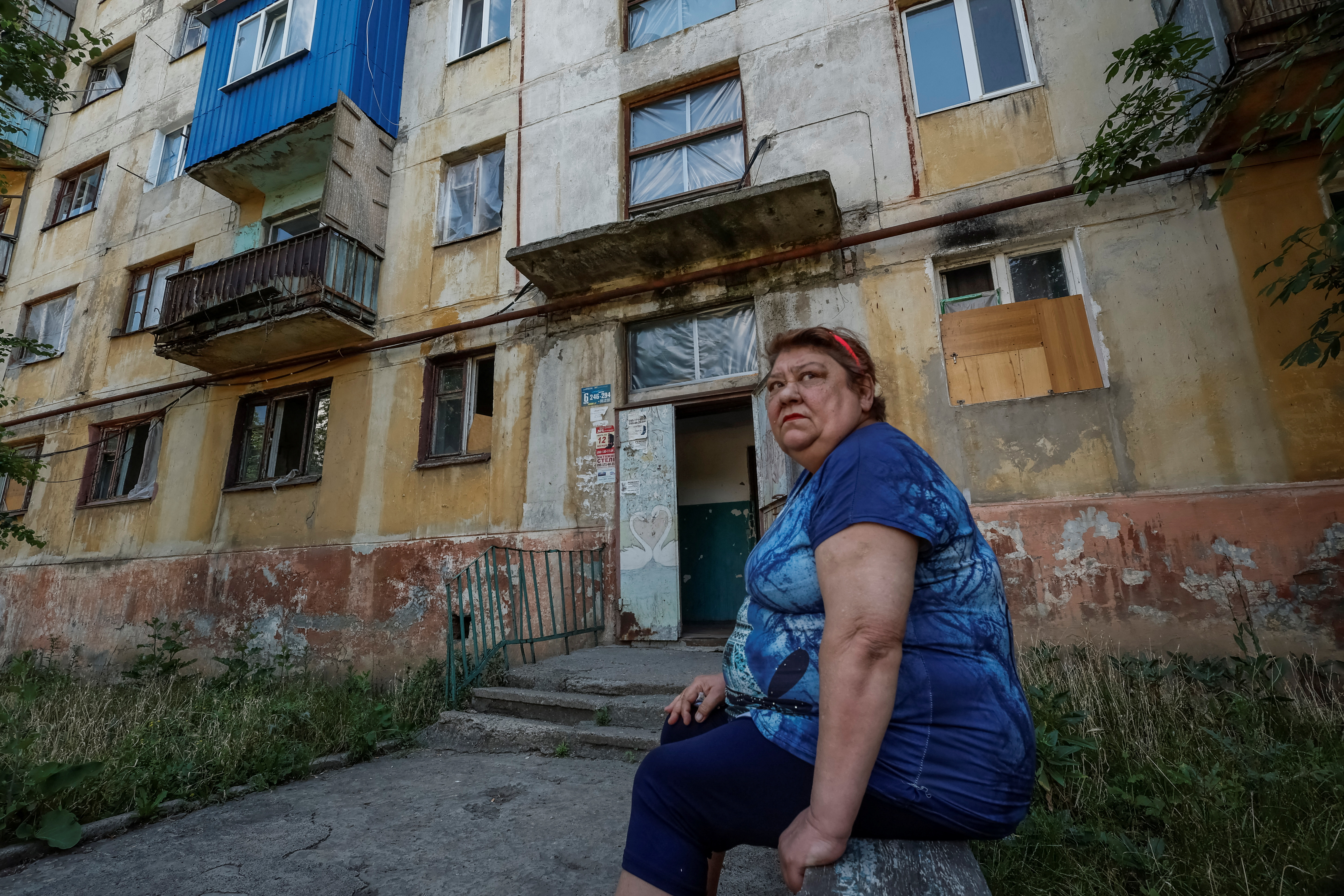 Alla, 64, a local resident, who got help from the Insulate Ukraine charitable organisation after she faced the consequences of a Russian military attack in her area, sits next to a residential building where she lives, amid Russia's attack on Ukraine, in the town of Mykolaivka, Donetsk region, Ukraine, June 18, 2024. REUTERS/Alina Smutko