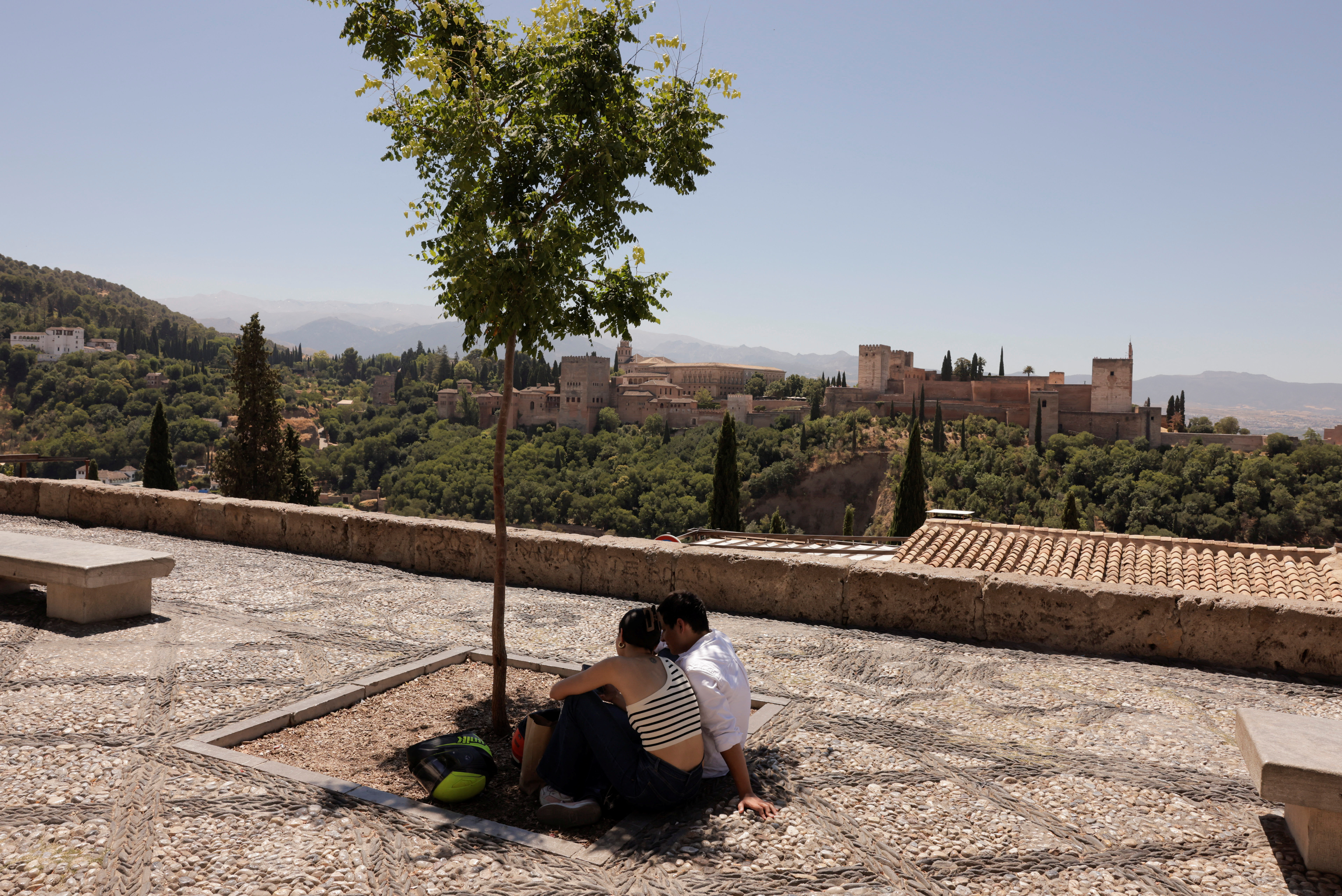 People sit as they hide from the strong midday sun under the shadow of a tree, 