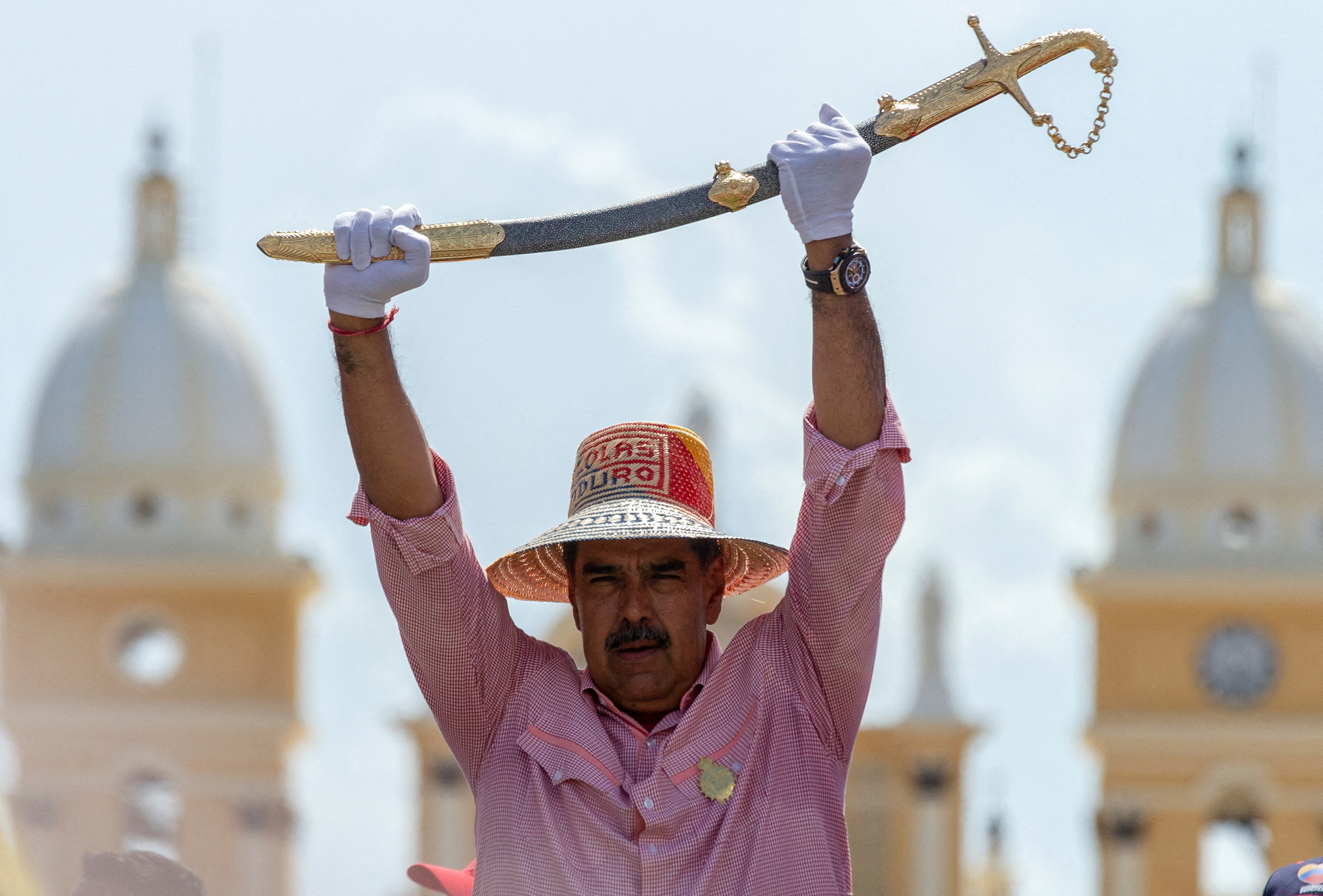 Nicolas Maduro in a straw hat lifts up a sword with white-gloved hands.