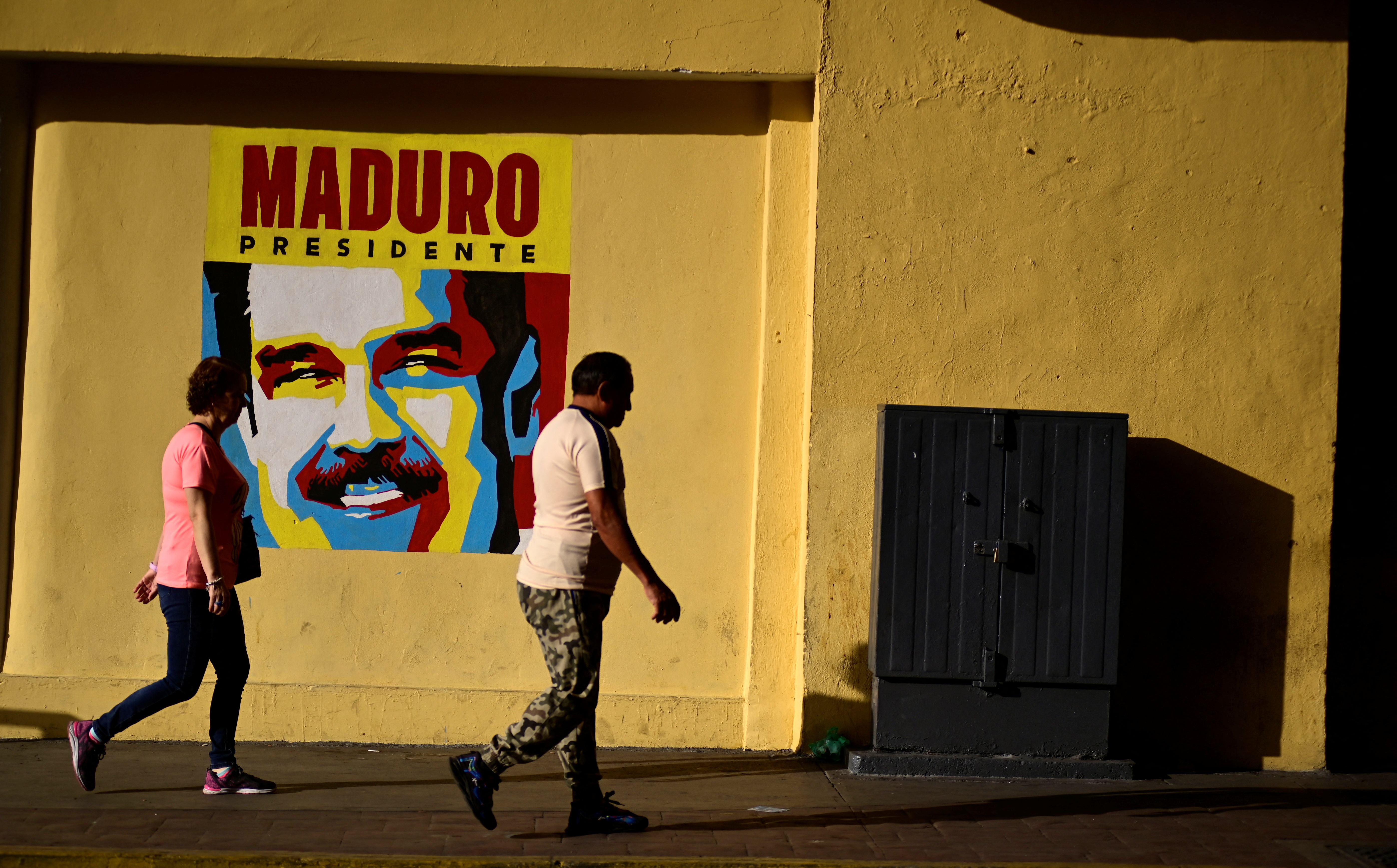 People walk past a poster of Nicolas Maduro