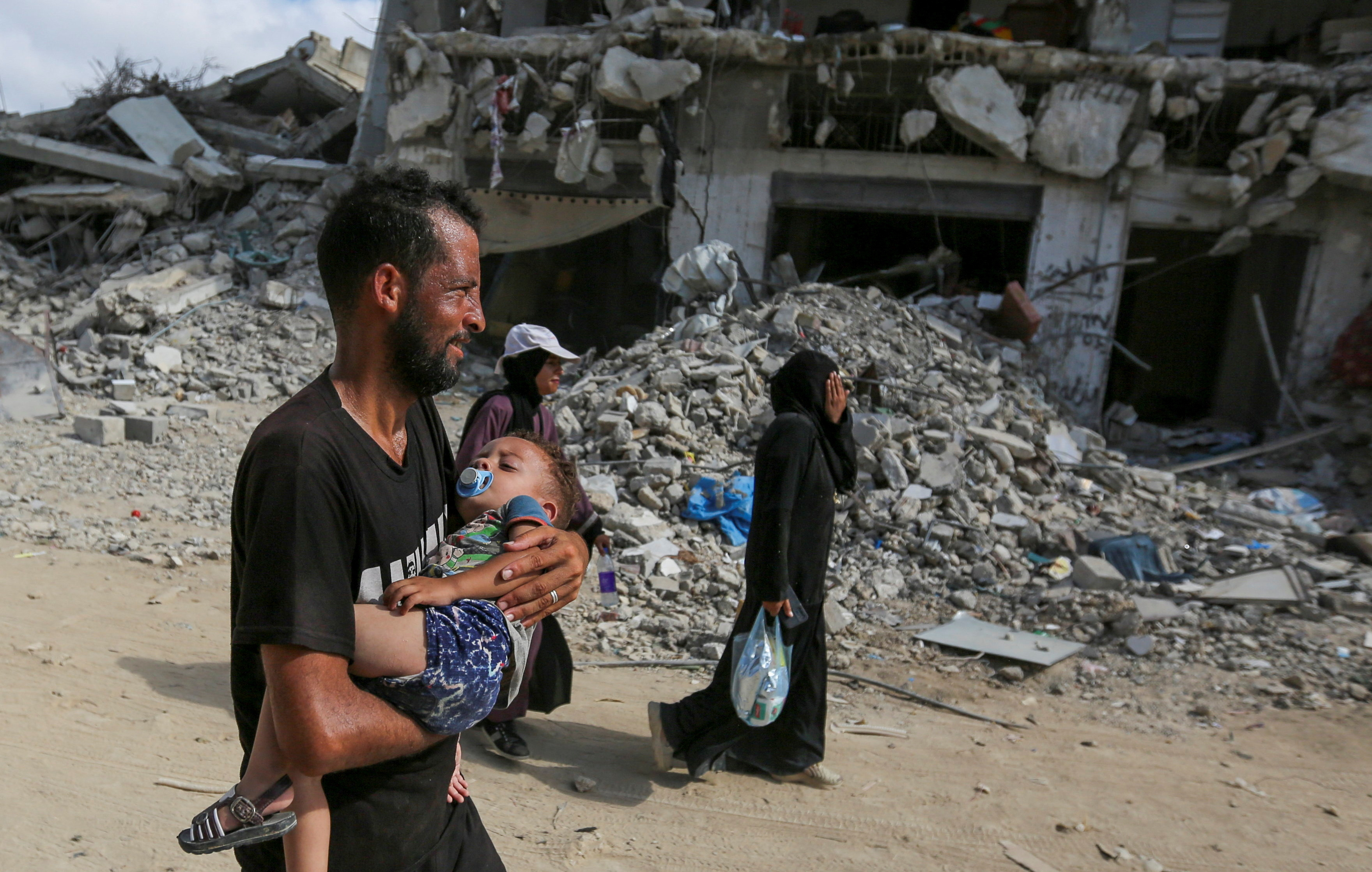 A Palestinian man carries a child, as Palestinians make their way to return to the eastern side of Khan Younis after Israeli forces pulled out from the area following a raid