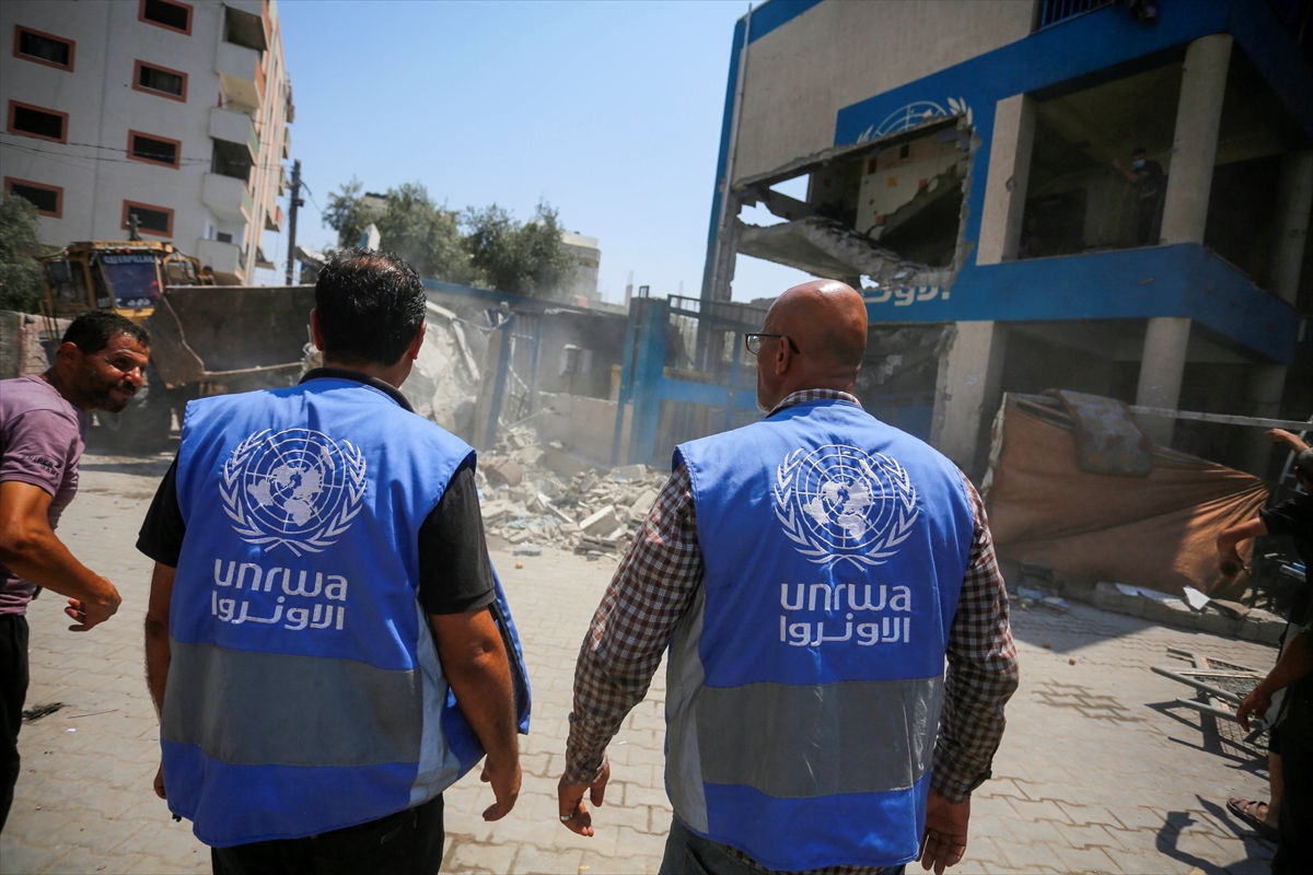 people wearing blue unwra vests walk towards a destroyed building