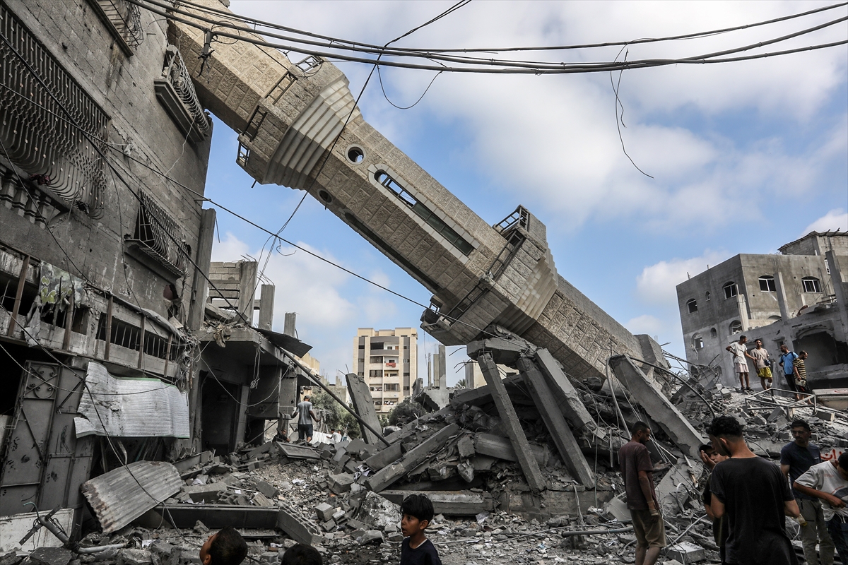 people inspect the remains of a collapsed building with a destroyed mosque tower lying on its side