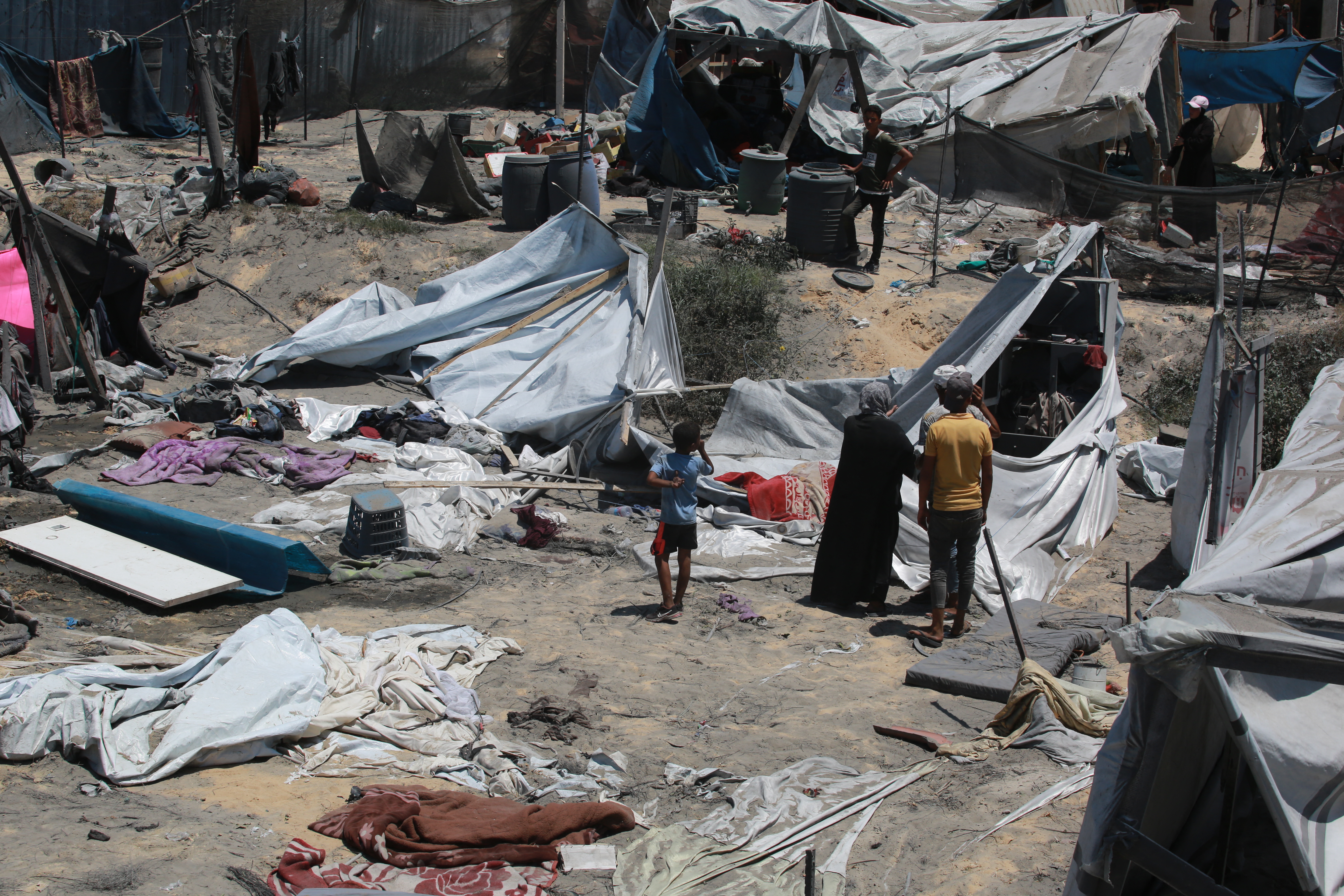 Palestinians look at the debris of tents following an Israeli military strike on the al-Mawasi camp for internally displaced people (IDP), near the city of Khan Yunis