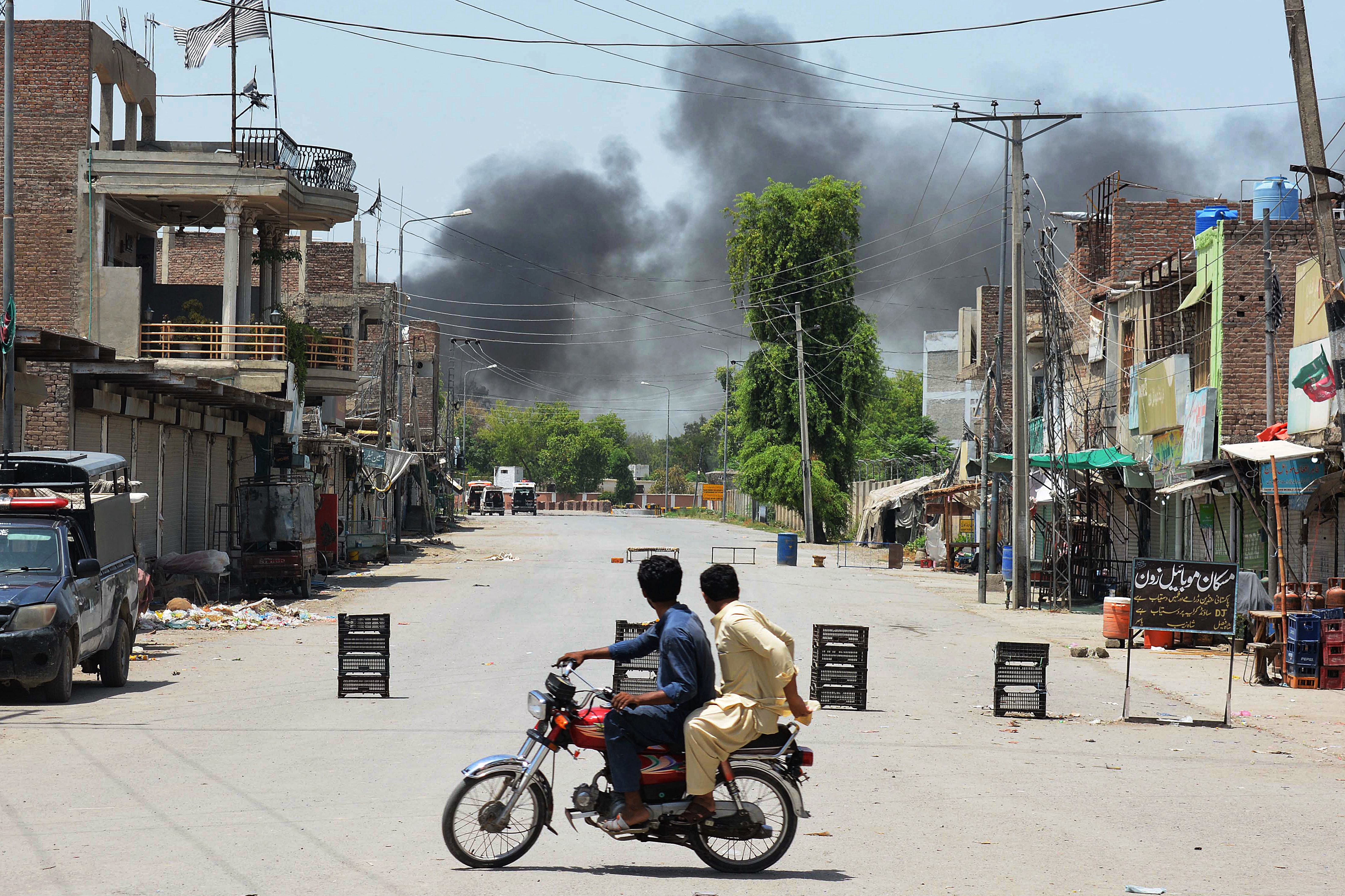 Men riding a bike watch as smoke rises following an explosion allegedly after militants suicide squad attempted to storm an army cantonment that houses military residences and offices in Bannu