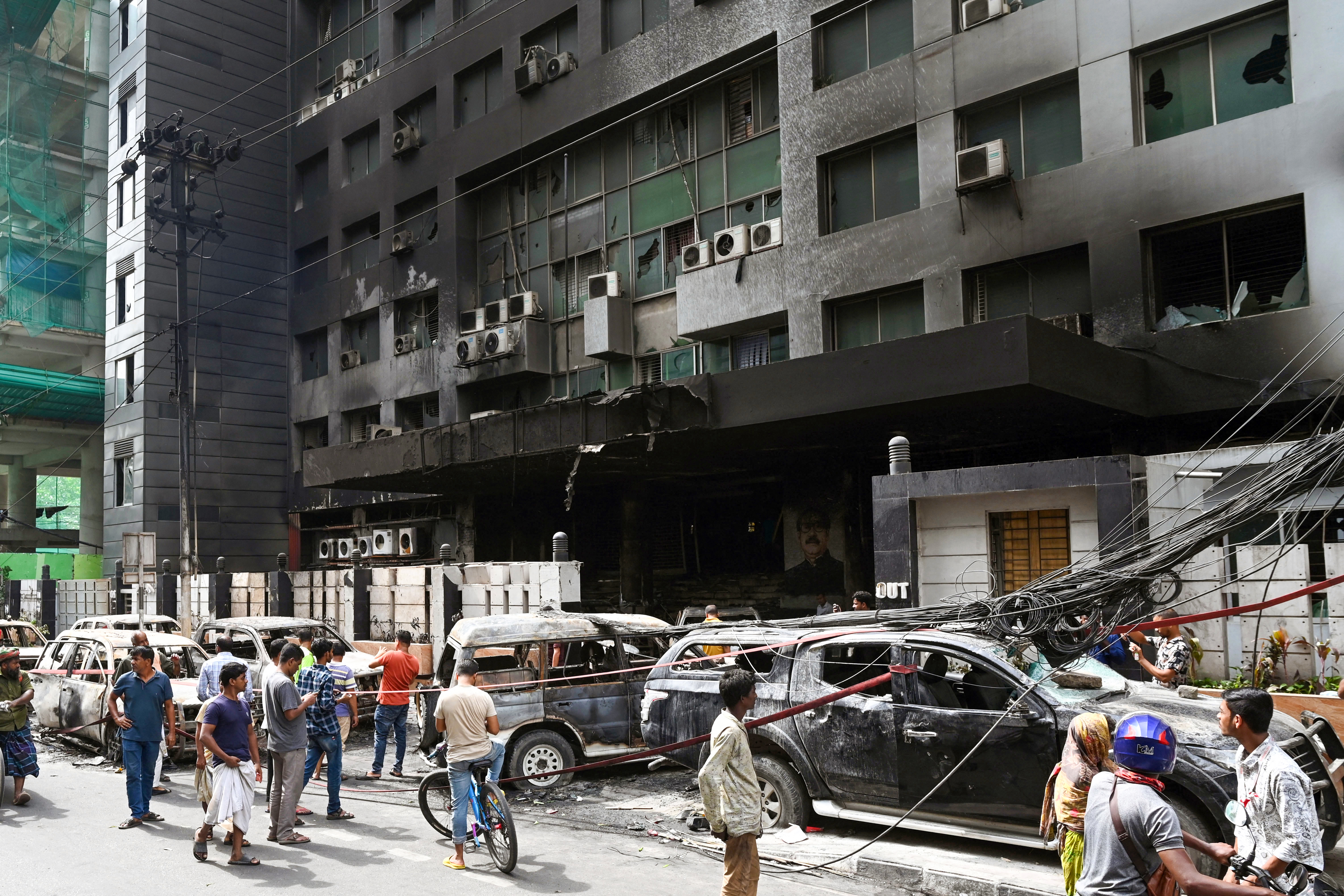 People walk past burnt vehicles after students set them on fire amid the ongoing anti-quota protest in Dhaka