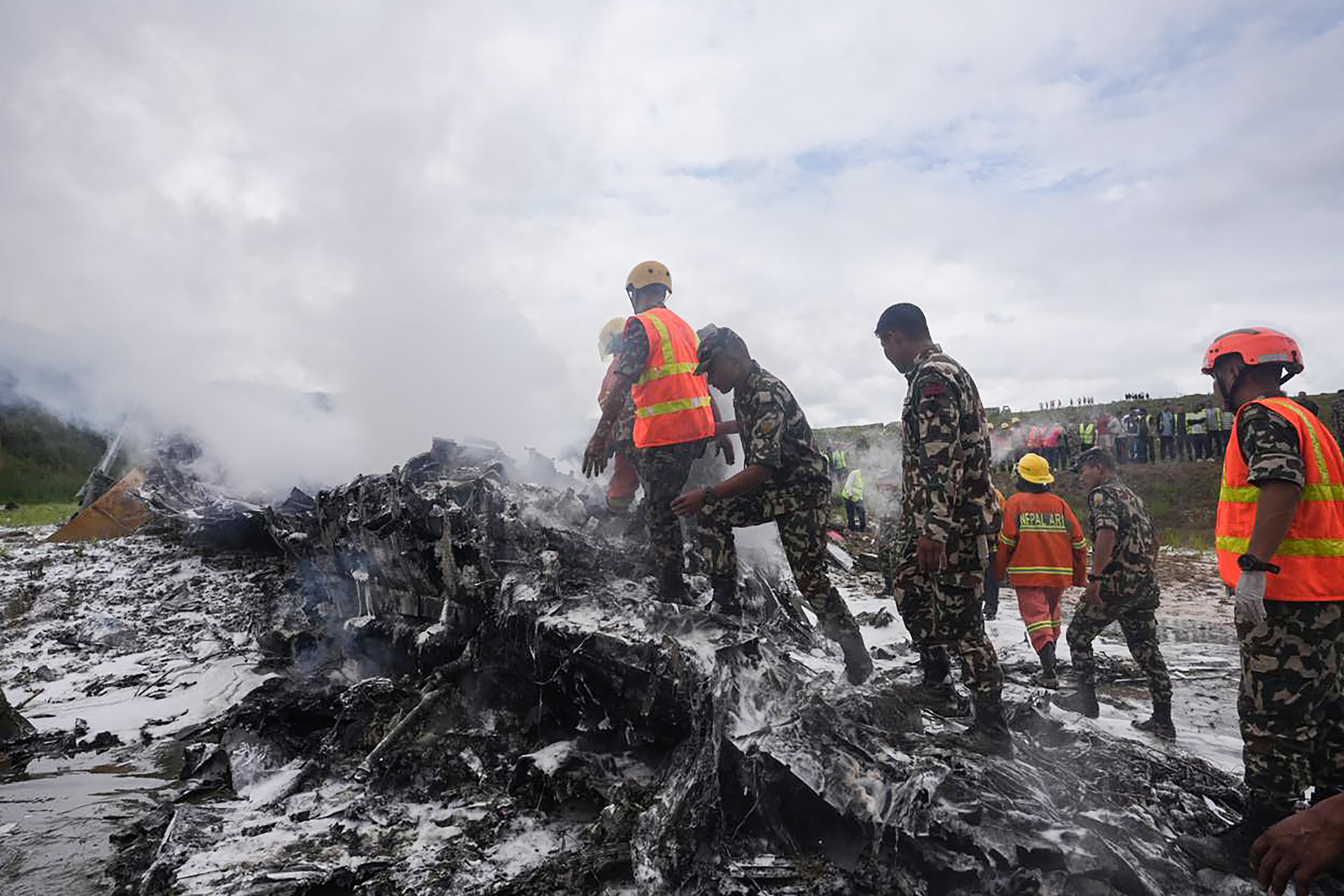 Rescuers and army personnel stand at the site after a Saurya Airlines' plane crashed during takeoff at Tribhuvan International Airport in Kathmandu on July 24, 2024. A passenger plane crashed on takeoff in Kathmandu on July 24, with the pilot rescued from the flaming wreckage but all 18 others aboard killed, police in the Nepali capital told AFP. (Photo by Prabin RANABHAT / AFP)