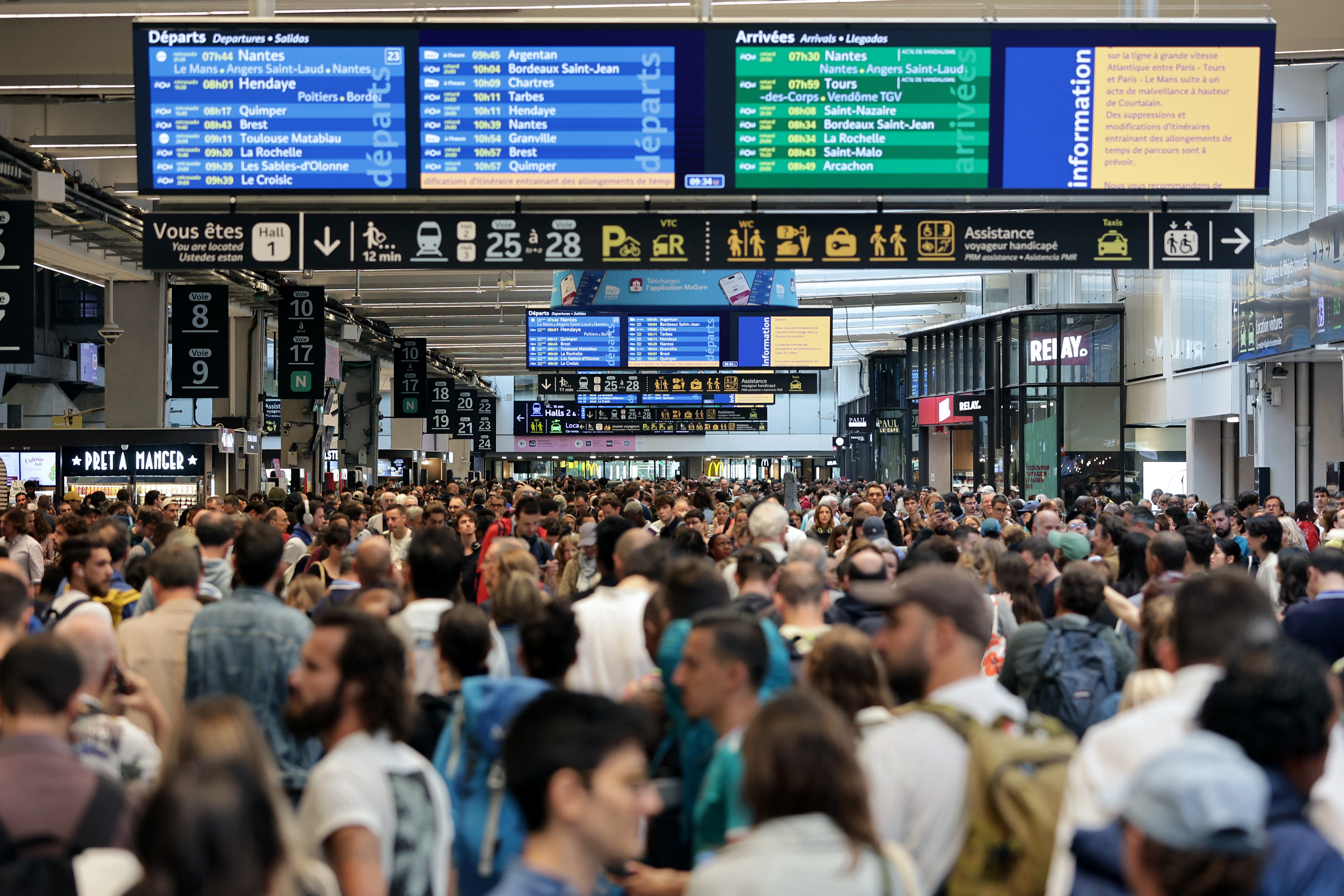 Passengers gather around the departure and arrival boards at the Gare Montparnasse train station in Paris