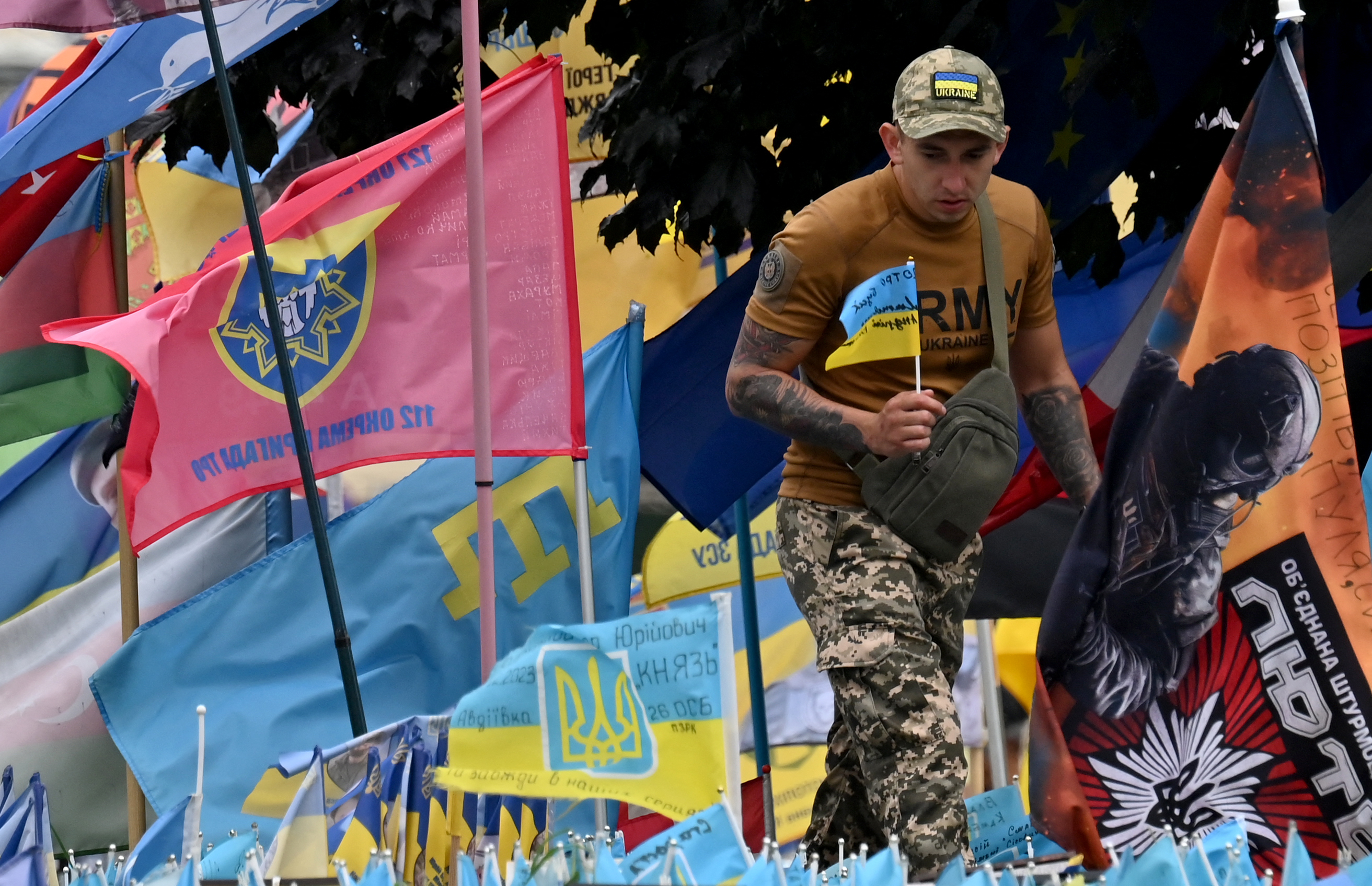 A Ukrainian solider places a Ukrainian flag at a memorial for those killed in the war. There are lots of flags around.