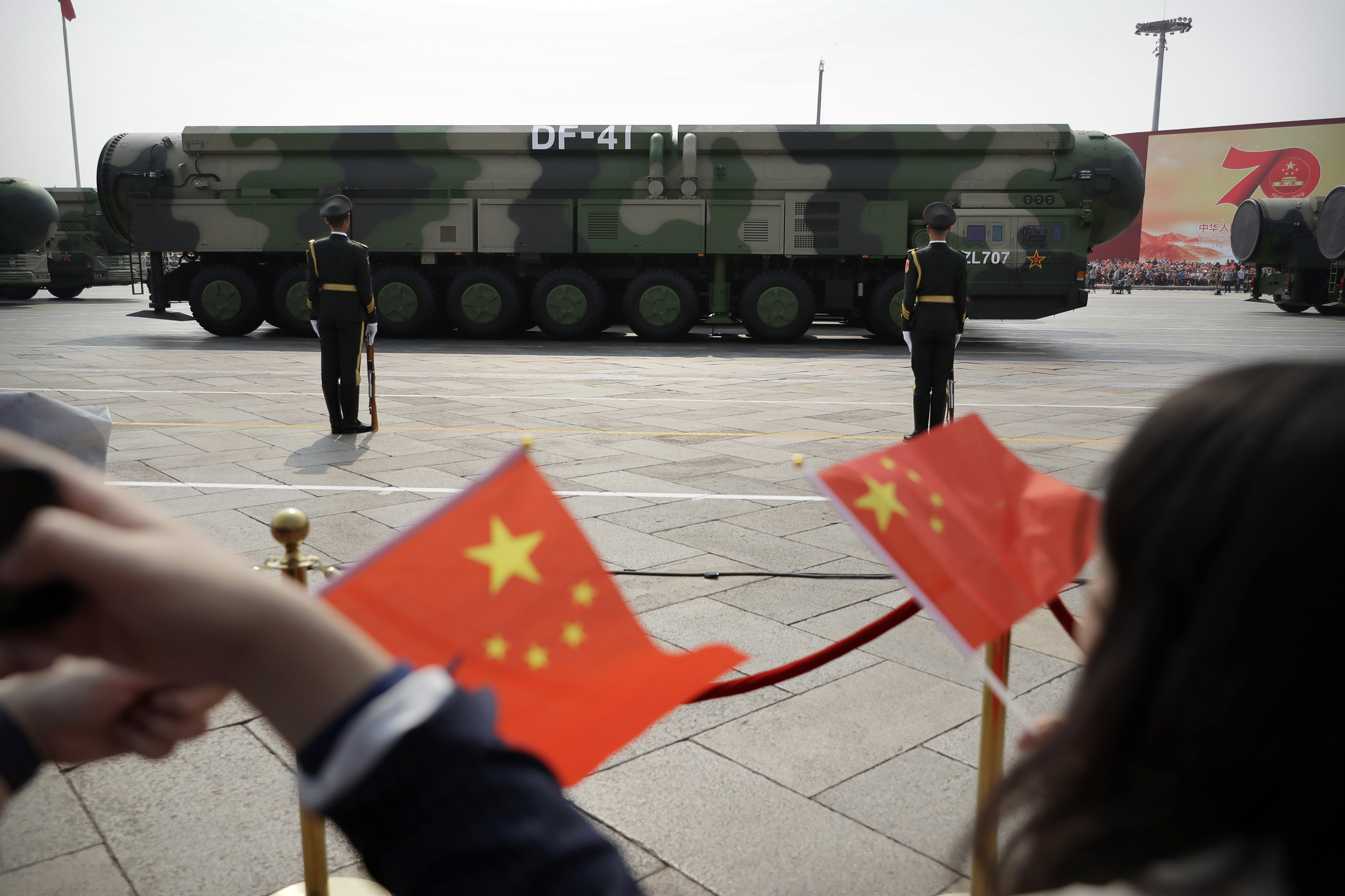 Spectators wave Chinese flags as military vehicles carrying DF-41 ballistic missiles capable of carrying nuclear warheads roll during a parade to commemorate the 70th anniversary of the founding of Communist China in Beijing, Oct. 1, 2019.
