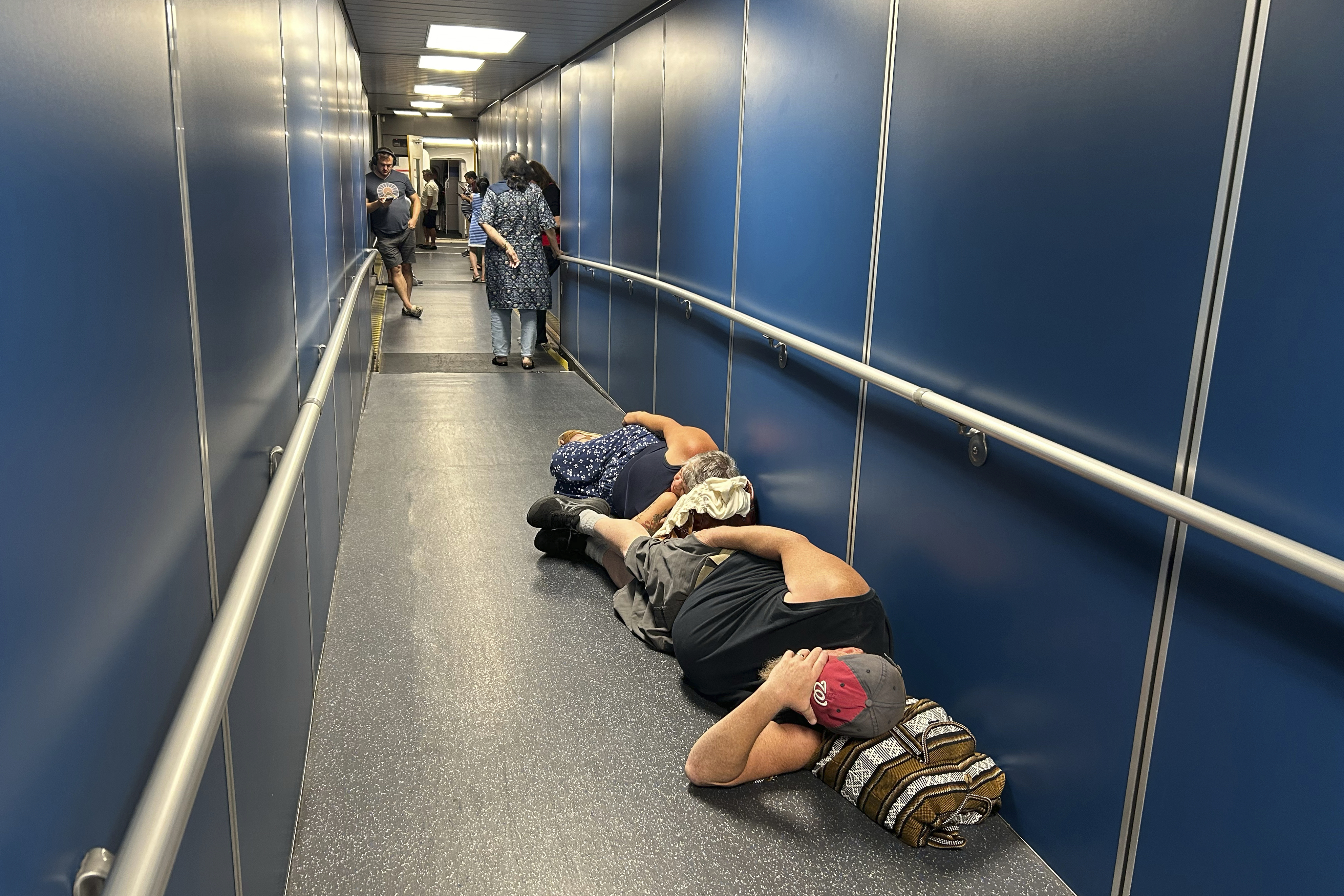 Travelers at Los Angeles International Airport sleep in a jetway for a delayed United Airlines flight to Dulles International Airport due to a widespread global outage