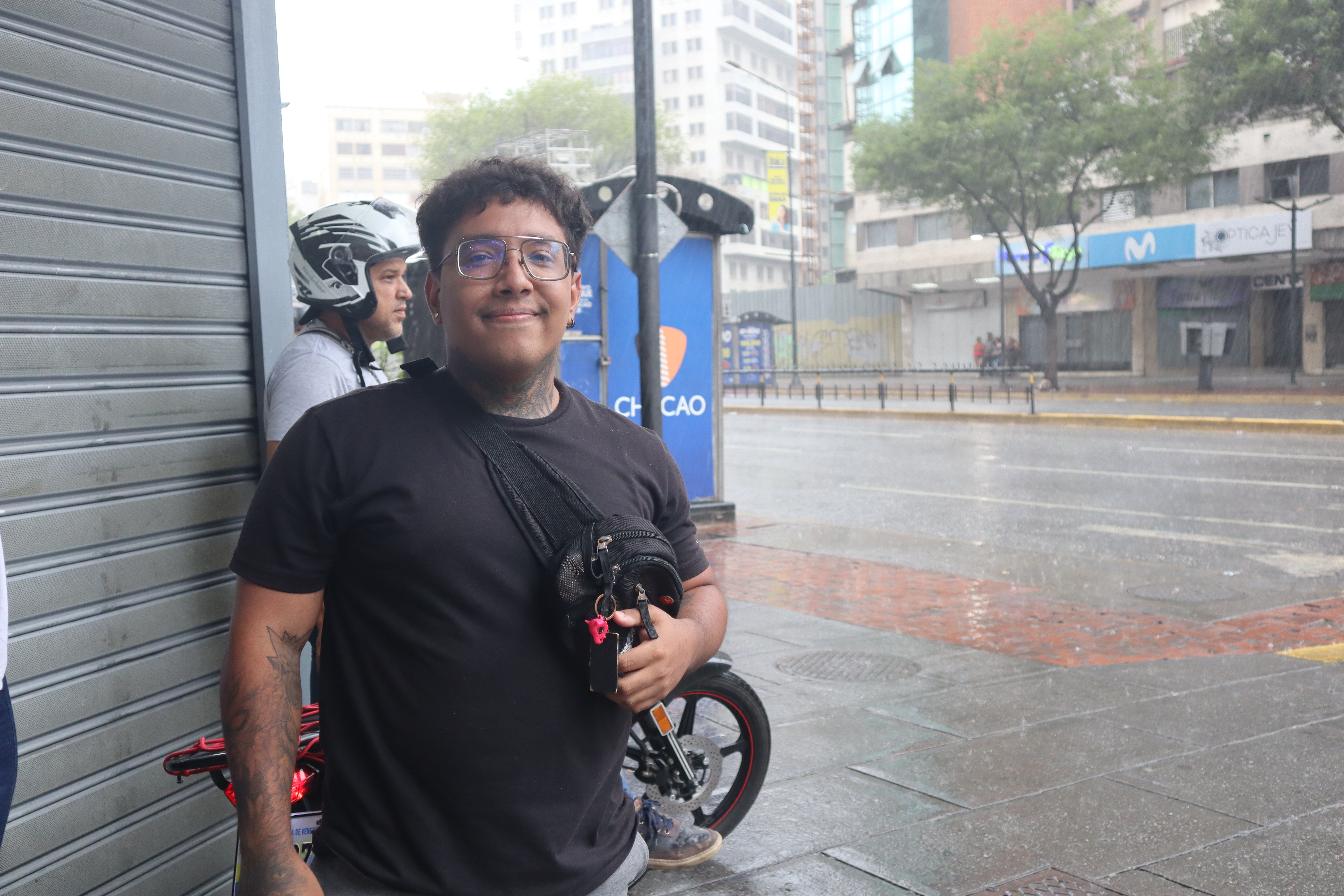 Cristian José Camacaro Guevara stands under an awning as rain pours on the street in Caracas.