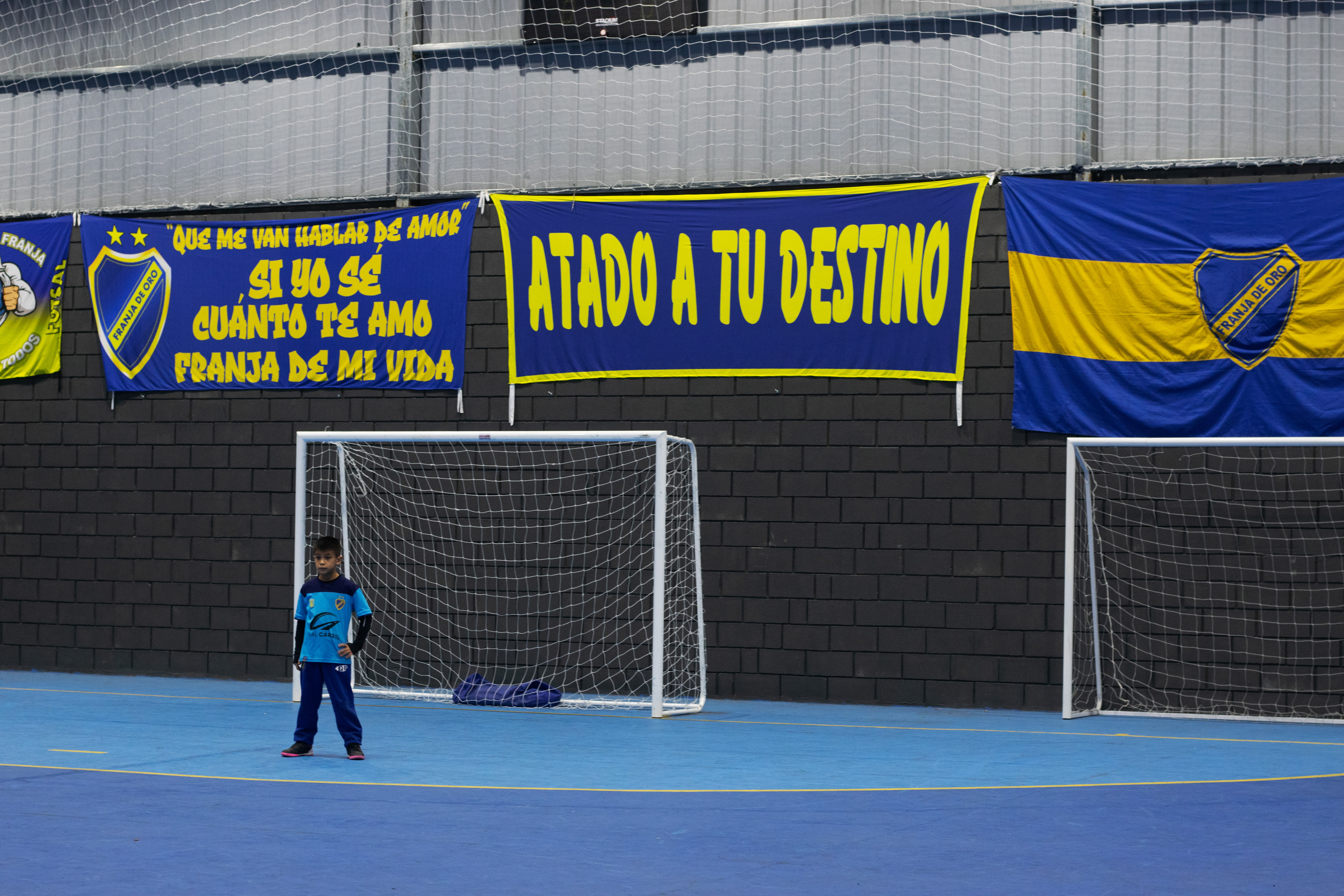 A child stands guard as goalie on an indoor soccer field.