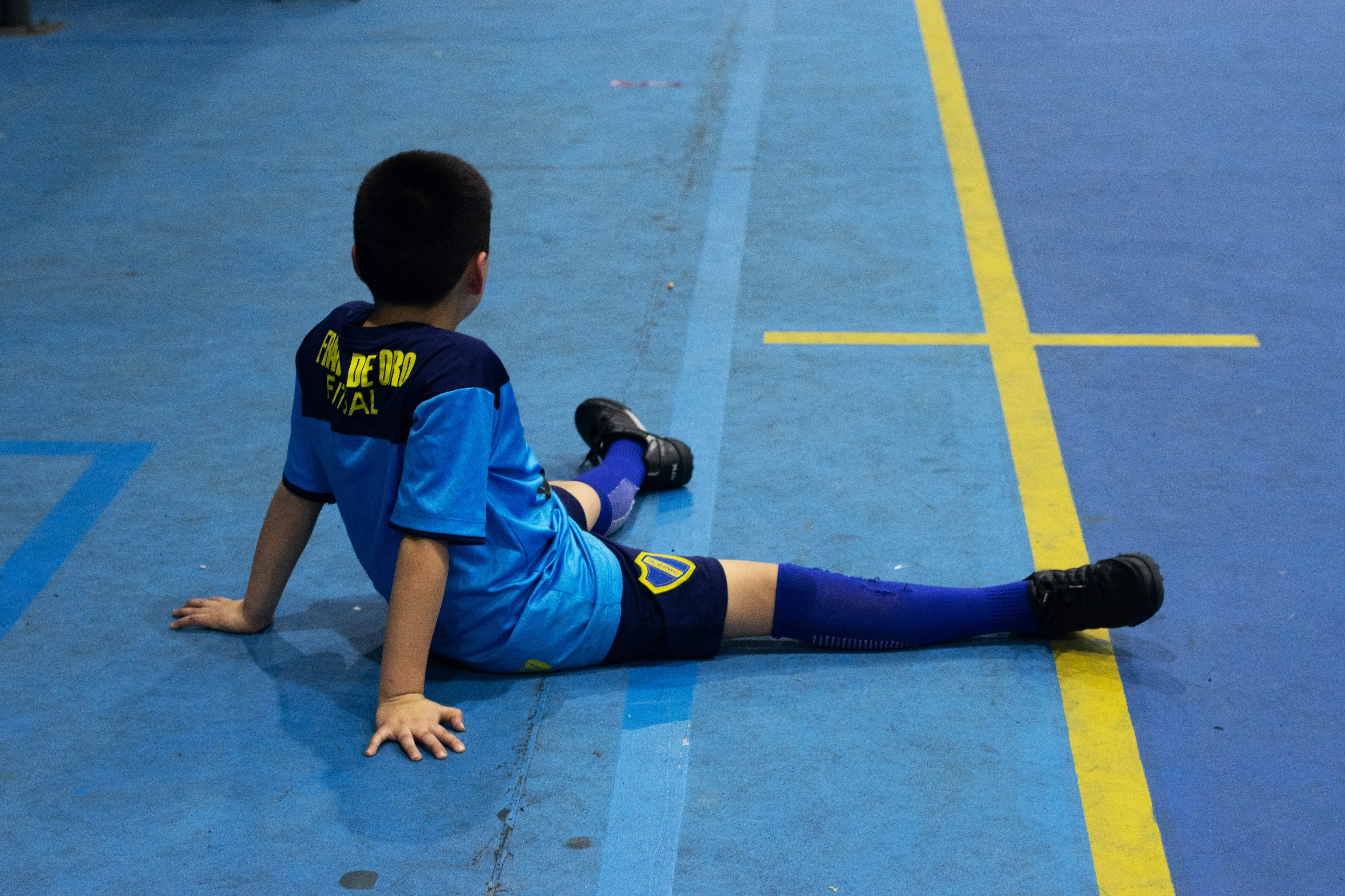 A boy from the Franja de Oro club sits on the floor of the indoor soccer field.