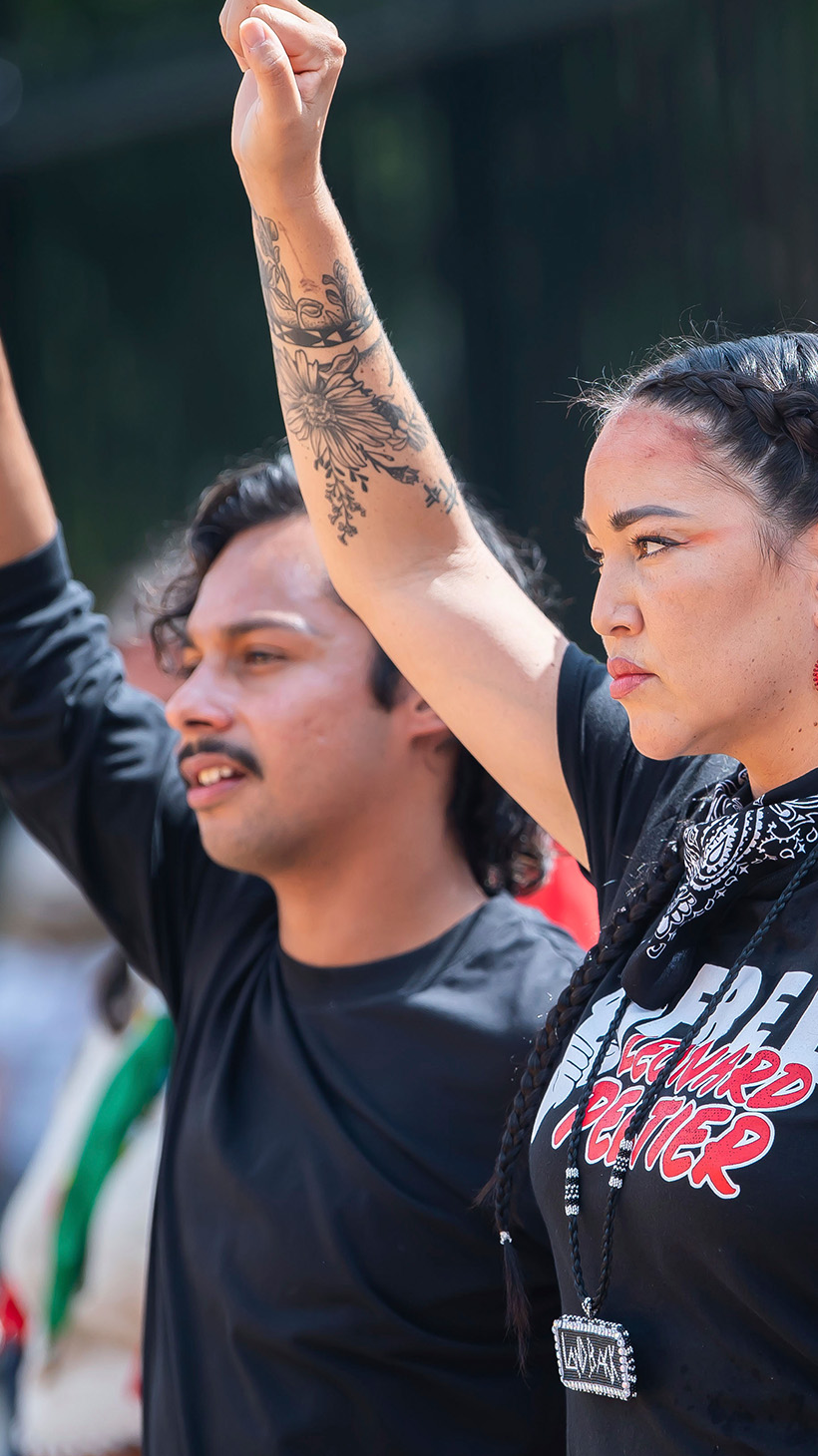 Indigenous activists raise a fist to show solidarity at an outdoor event to call for Leonard Peltier's release.