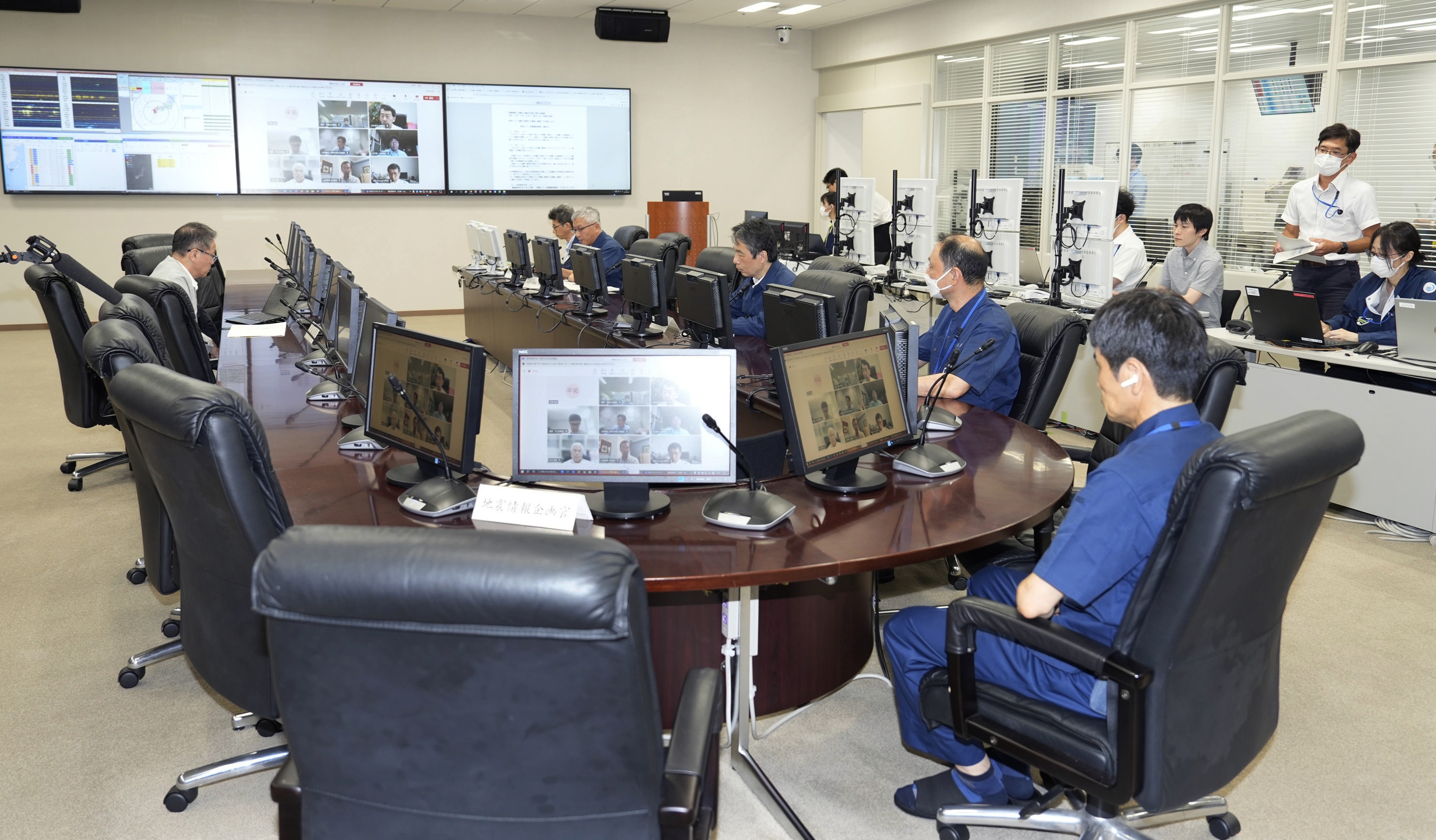 People sitting around a table at Japan's meteorological agency, There are large screens on the wall behind them and at the desks.