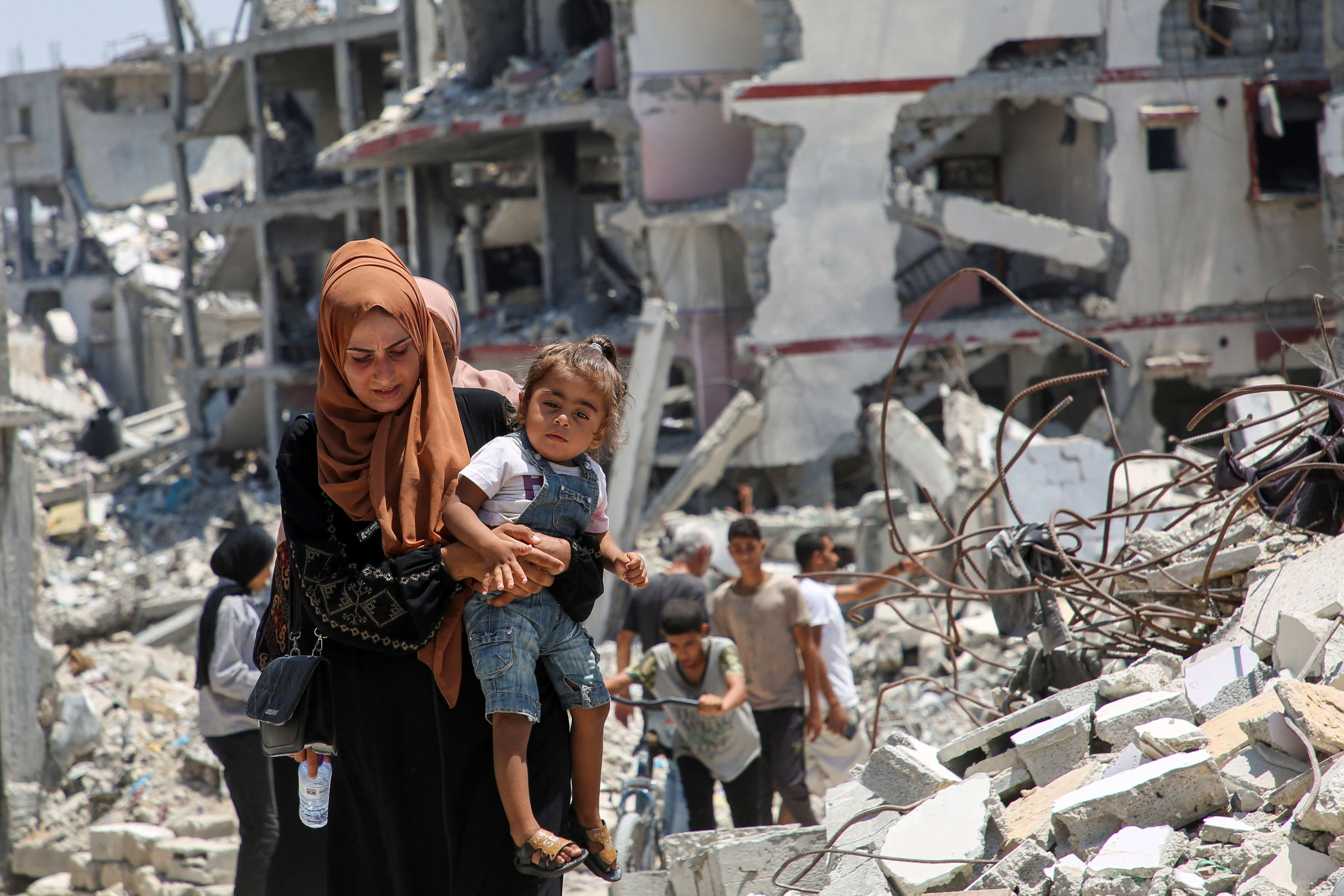 A Palestinian woman holds her daughter as she walks past the rubble of houses destroyed during the Israeli military offensive, amid Israel-Hamas conflict, in Khan Younis in the southern Gaza Strip July 10, 2024. REUTERS/Hatem Khaled