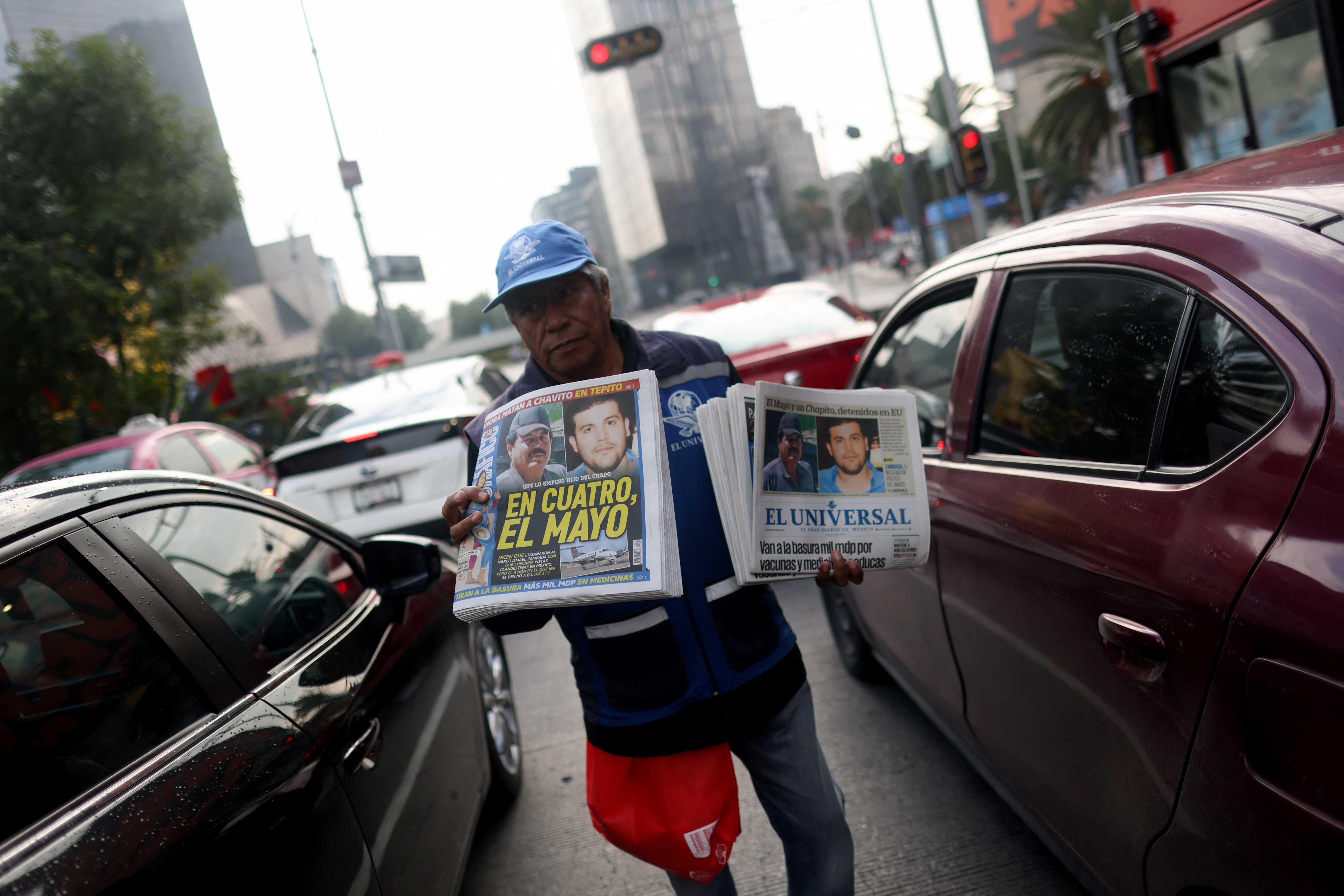 A newspaper vendor sells papers as he walks between cars stuck in traffic in Mexico City. The newspapers announce the arrest of the drug lord "El Mayo"