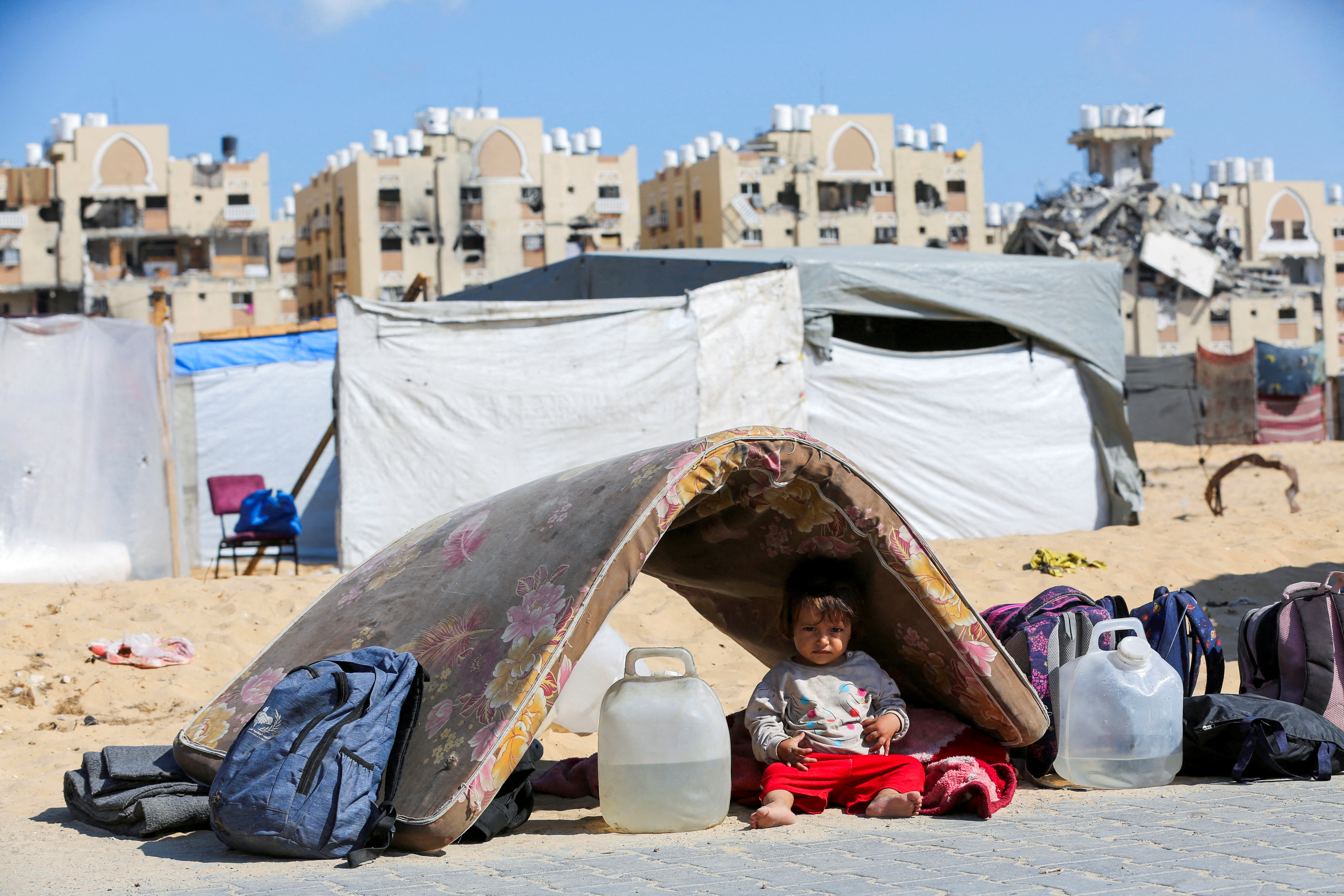 A displaced Palestinian girl sits under a mattress