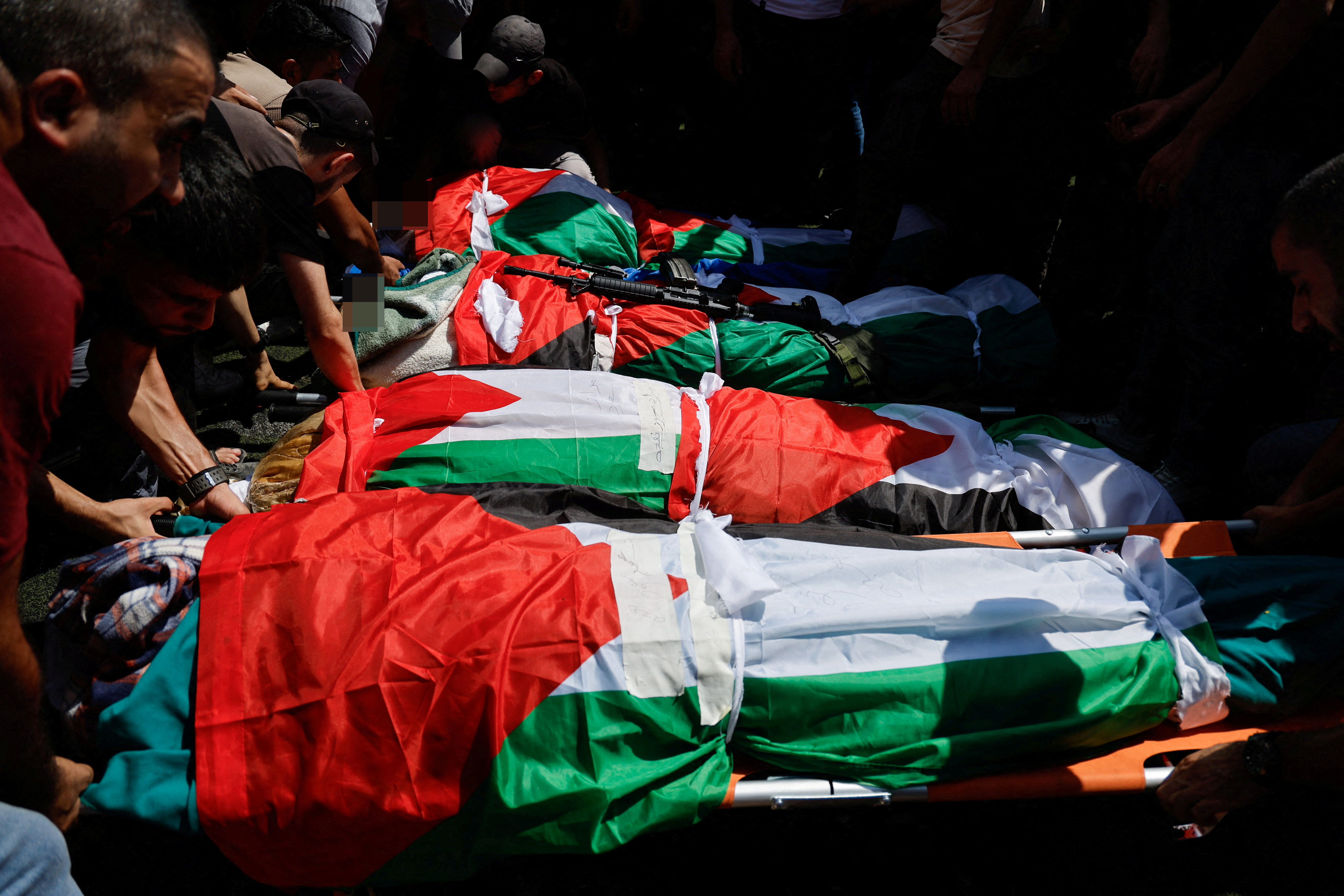 Mourners stand next to the bodies during a funeral of four Palestinians killed in an Israeli airstrike on Al-Faraa camp