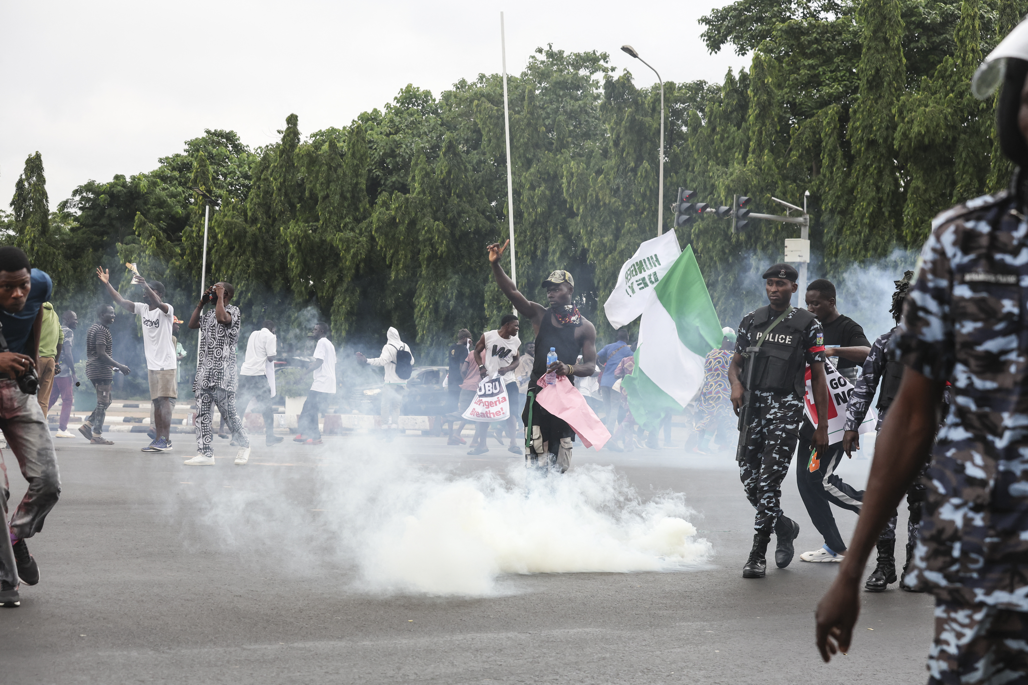 Demonstrators react as Nigerian policemen fire tear gas canisters during the End Bad Governance protest in Abuja