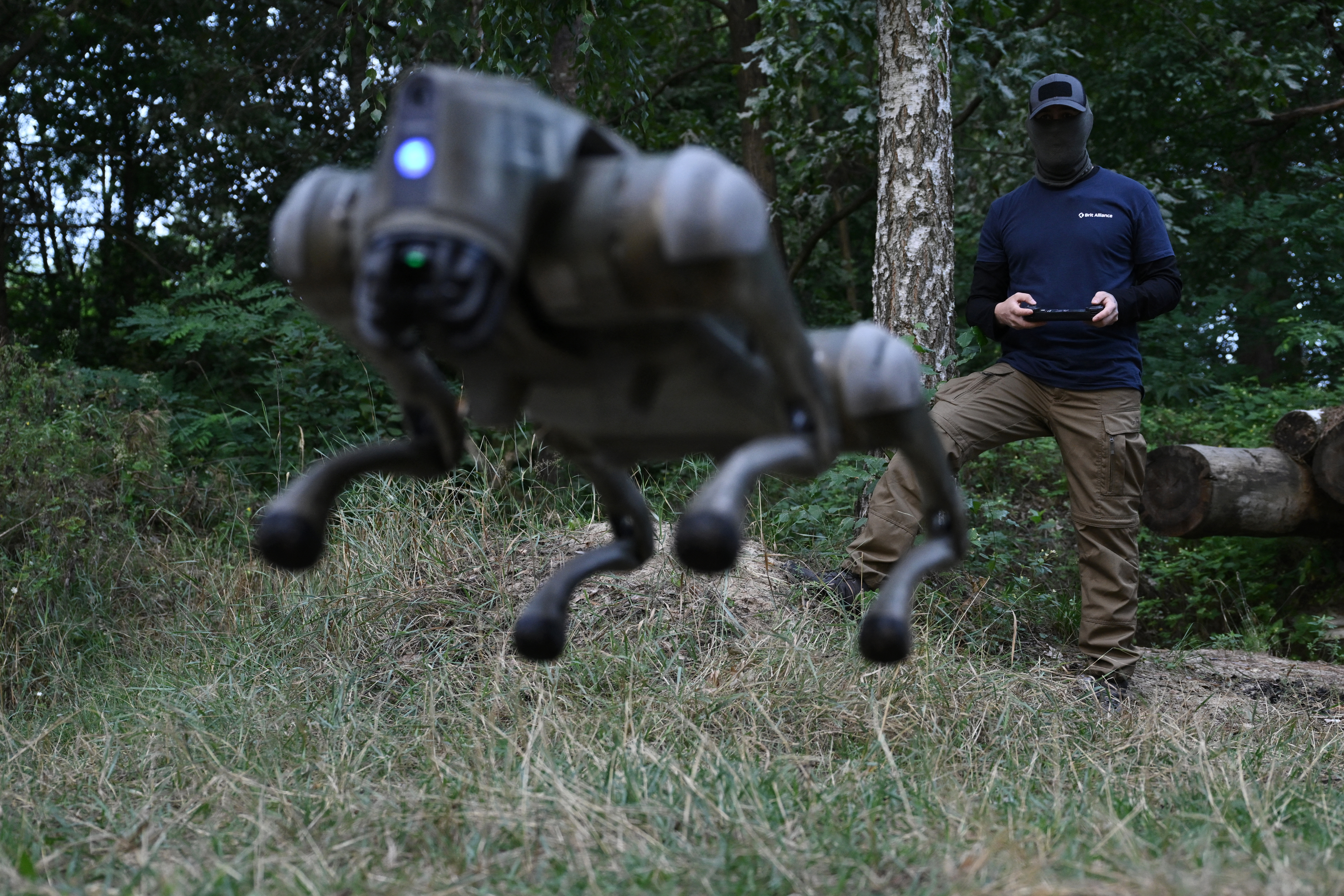 A robot dog leaping into the air. The Ukrainian soldier controlling it is standing in the background.