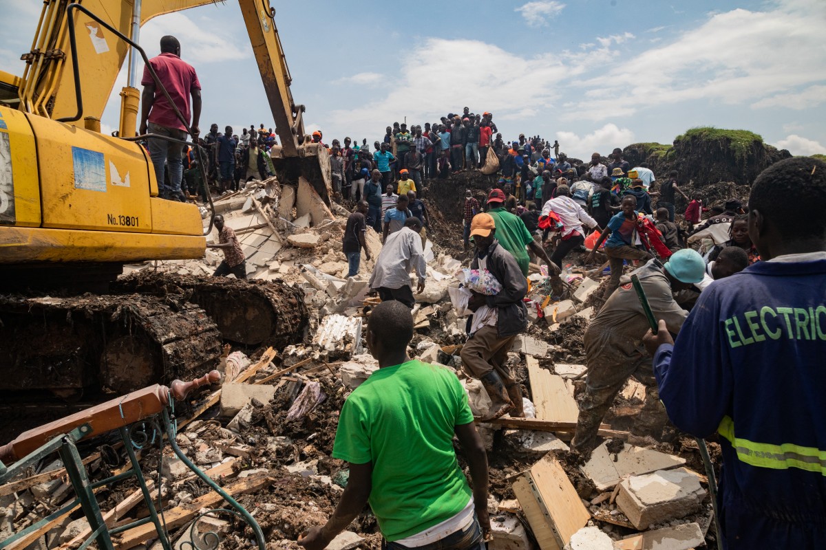 People look on as an excavator helps search for people trapped under debris after a landfill collapsed in Kampala on August 10, 2024. - Eight people including two children were killed when a landfill in the Ugandan capital Kampala collapsed, the city authority said. (Photo by BADRU KATUMBA / AFP)