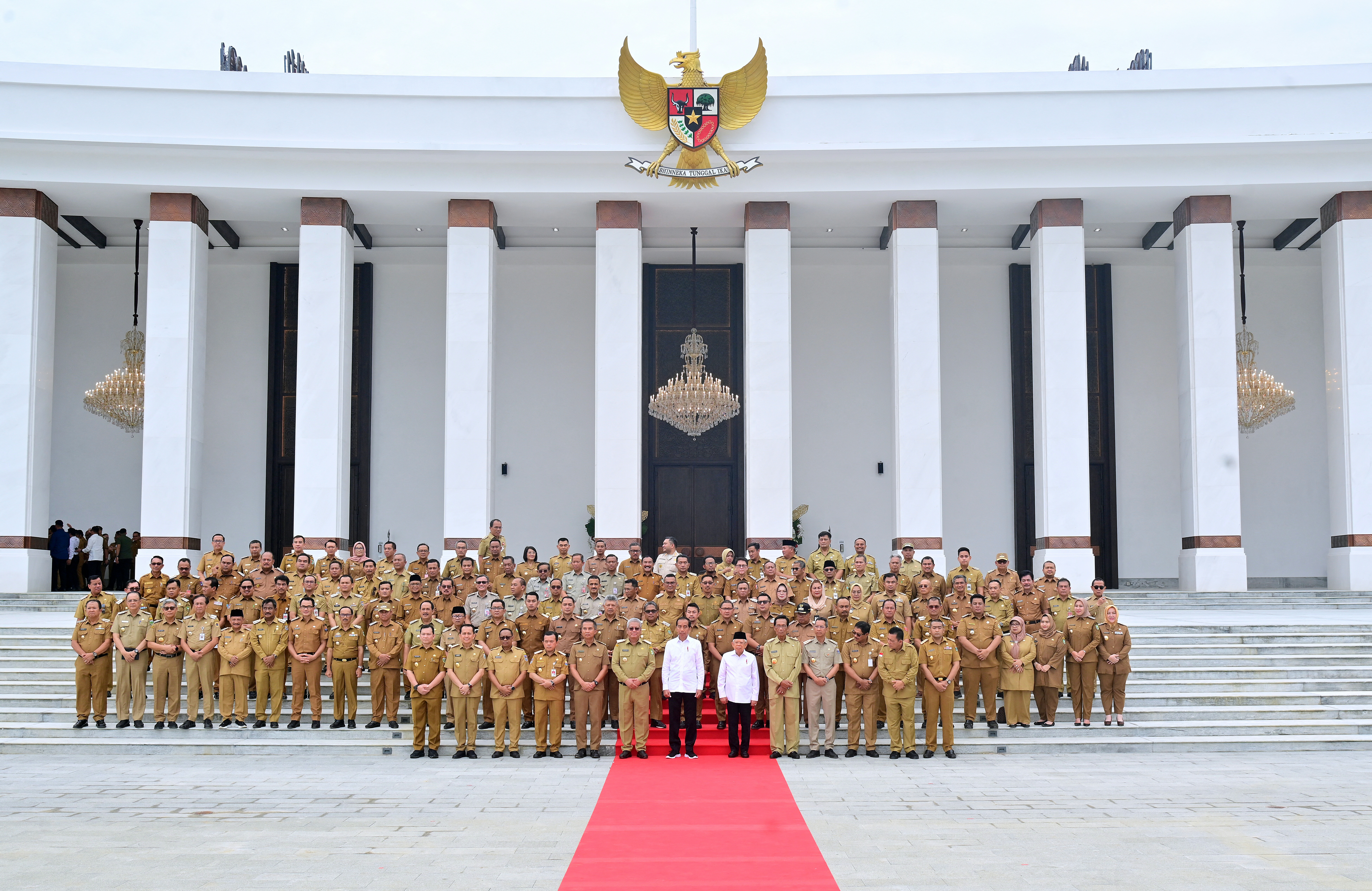 Indonesia's cabinet standing outside the new presidential palace in Nusantara. The buiding is behind them. It looks vast with tall white columns. The Indonesian insignia is on the roof