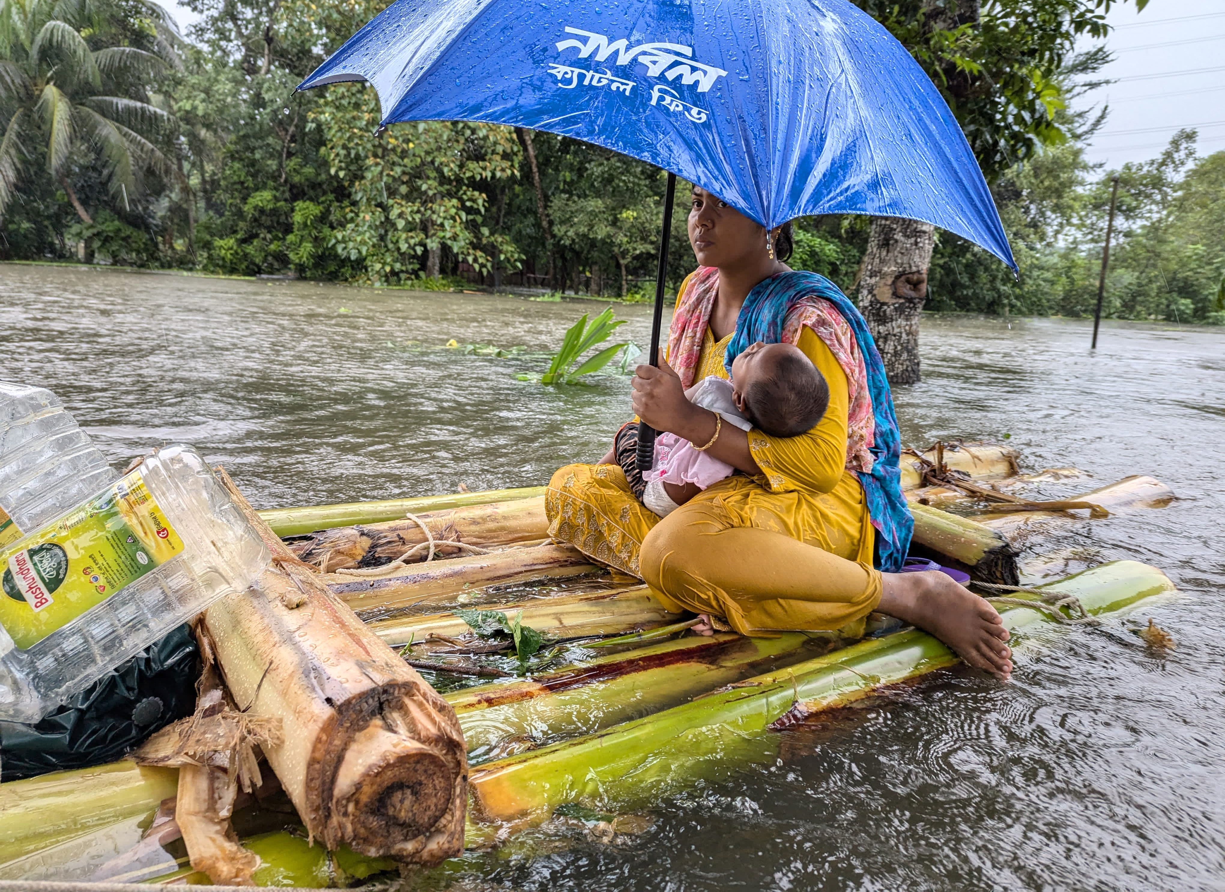 A woman and her child wade through flood waters in Feni