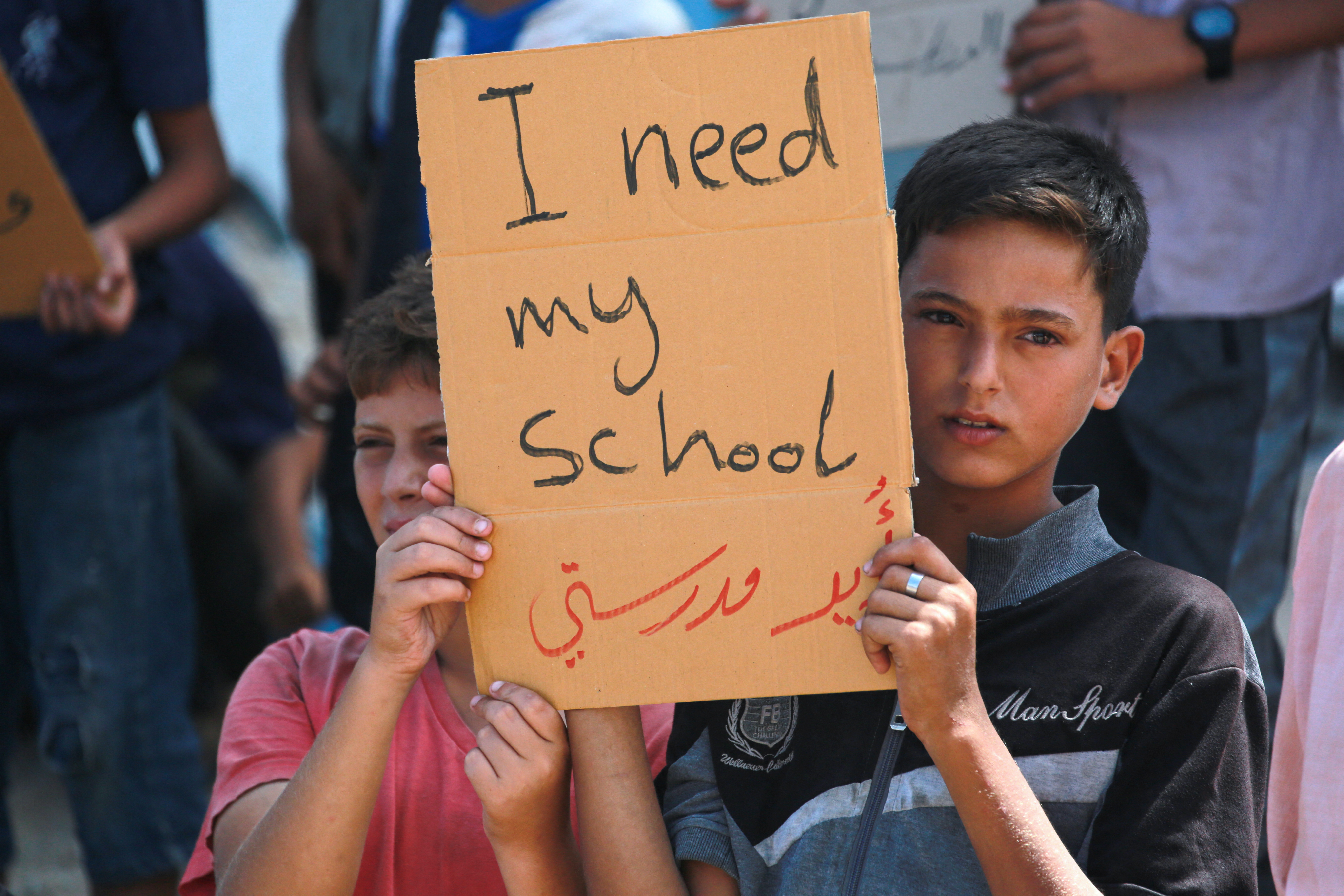 Palestinian children lift placards during a protest calling for an end of the Gaza conflict and a return to school ahead of the new academic year, next to a damaged school building in Khan Yunis in the southern Gaza Strip on August 28, 2024.