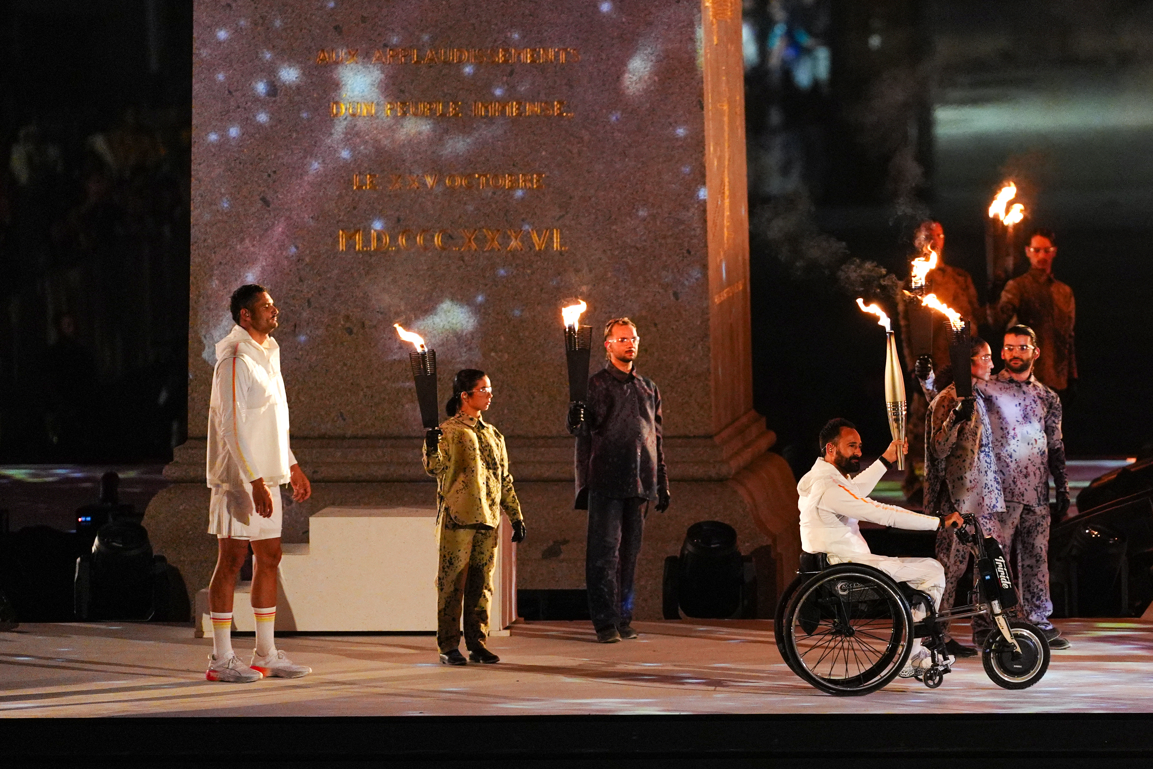 France's wheelchair tennis player Michael Jeremiasz (2nd R) holds the Paralympic flame next to France's Olympic flag bearer Florent Manaudou (L) during the torch relay as part of the Paris 2024 Paralympic Games Opening Ceremony at the Place de la Concorde in Paris on August 28, 2024. (Photo by Dimitar DILKOFF / AFP)