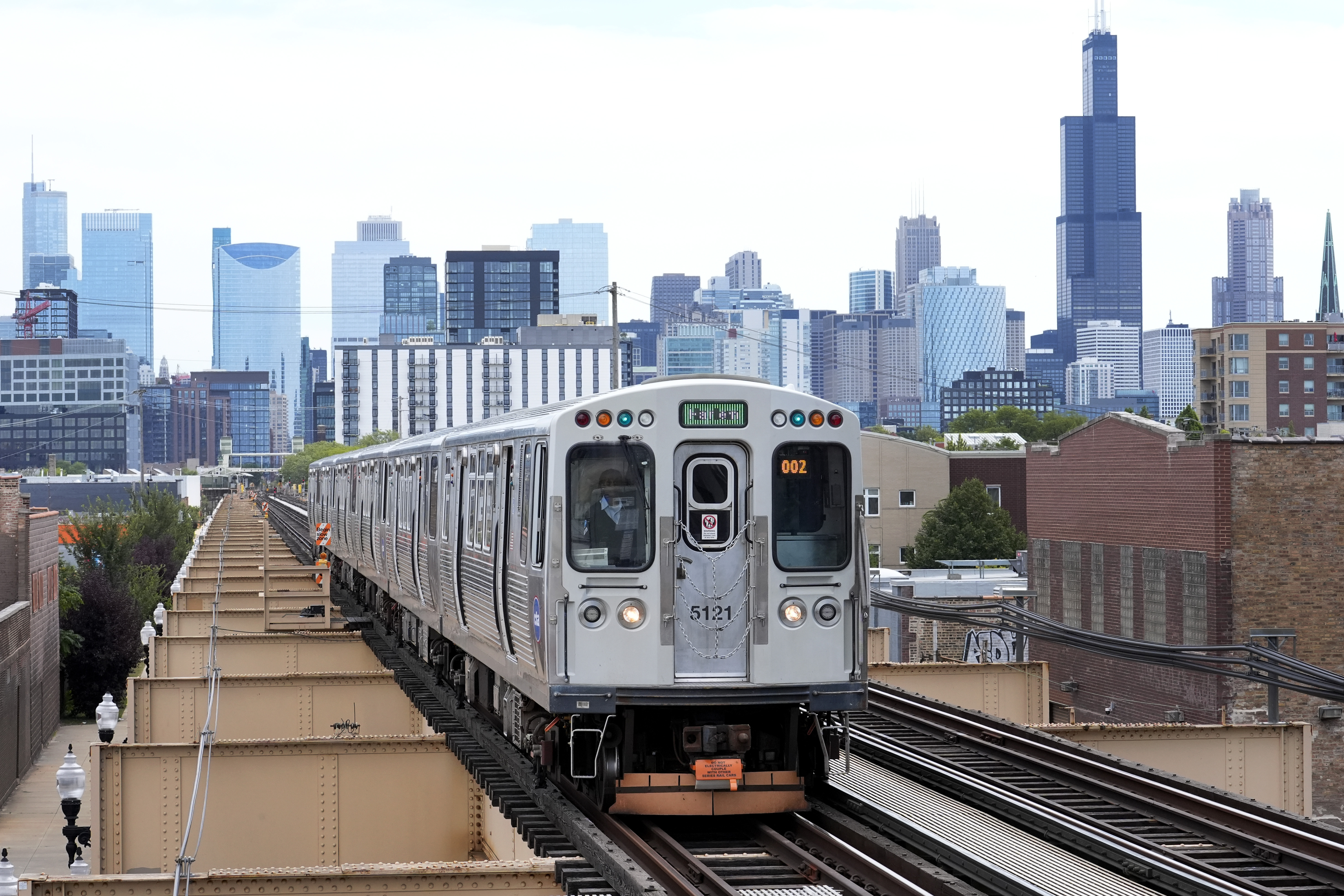 The Chicago El train travels across an elevated rail line with the city skyline in the background.