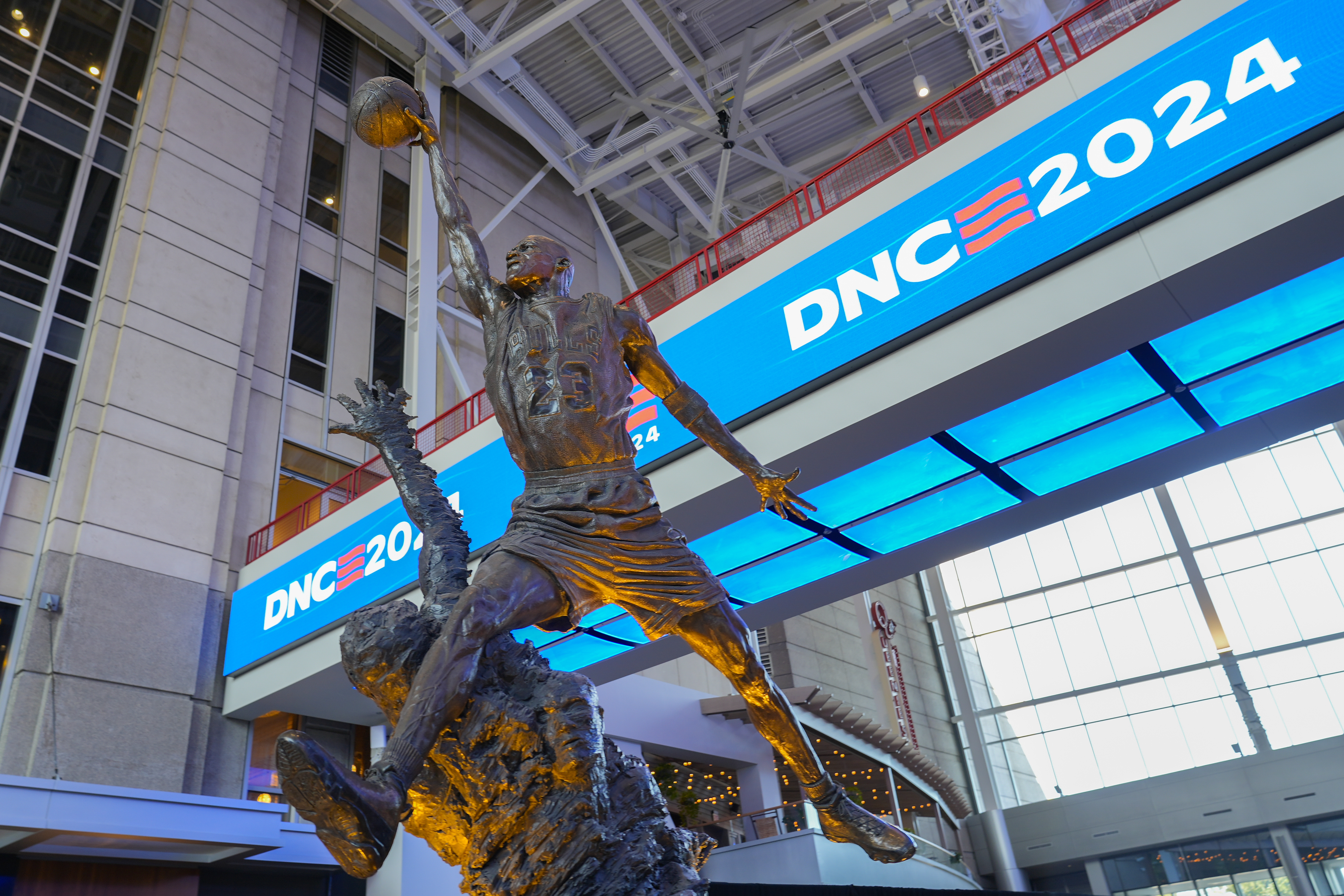 A Michael Jordan statue — showing the basketball player in mid-air, preparing to dunk — stands in front of an LED sign that advertises the phrase "DNC 2024"