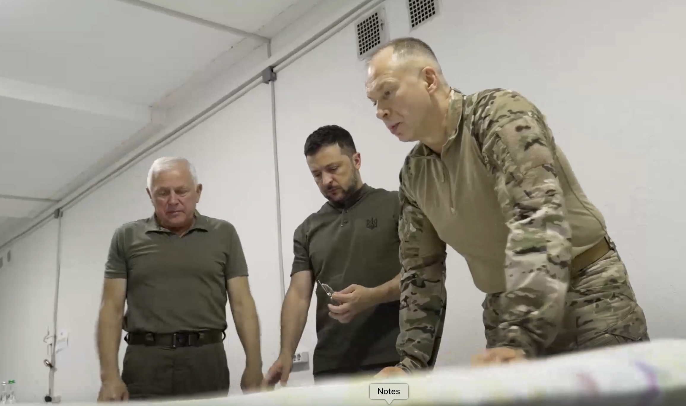 Volodymyr Zelenskyy discussing the war with his top commanders. They are standing over a desk and looking at a map