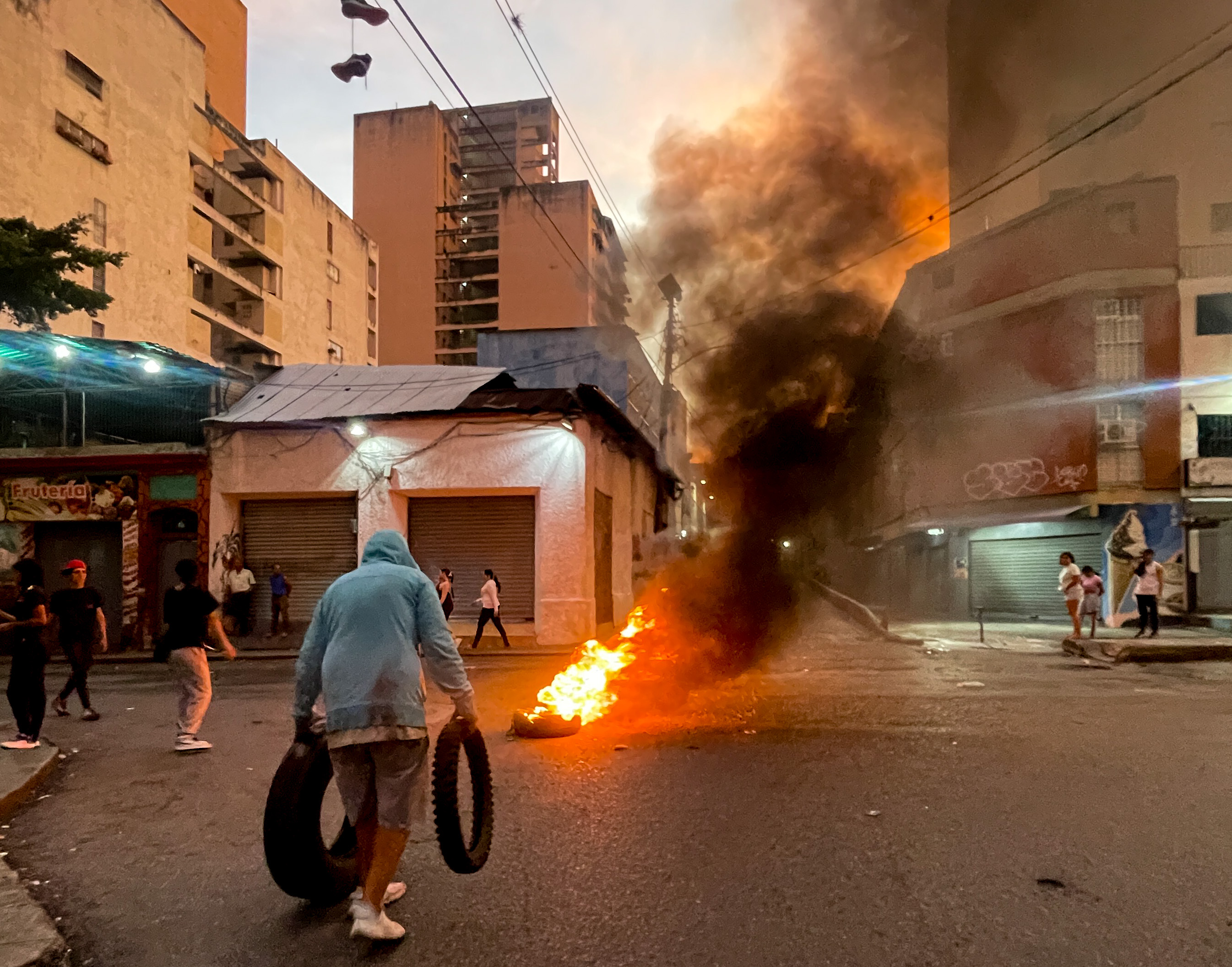 A protester carries tires, while another tire burns in the distance.